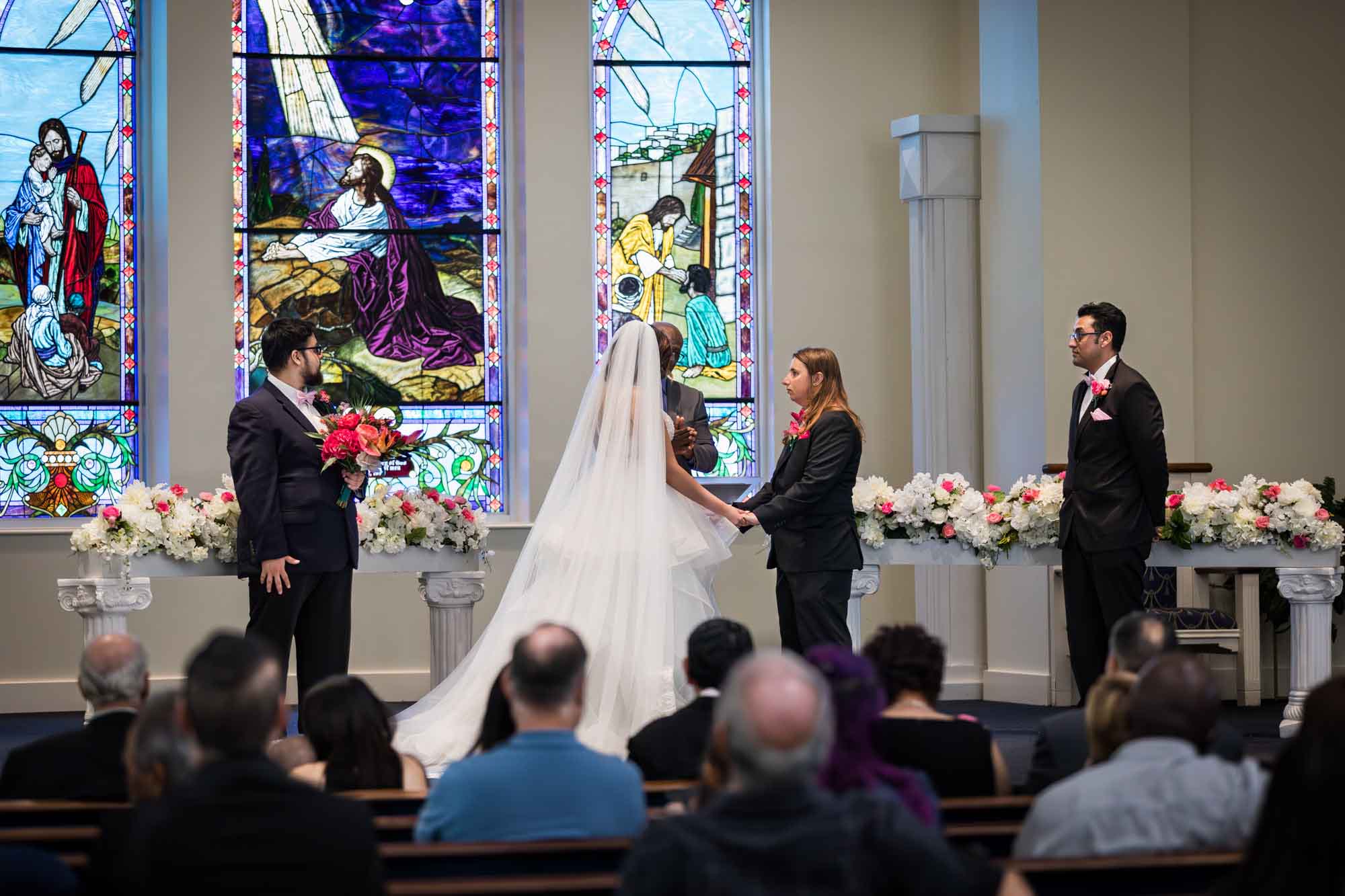 Cornerstone Church wedding photos of bride and groom holding hands during ceremony with stained glass windows in background and guests seated in pews