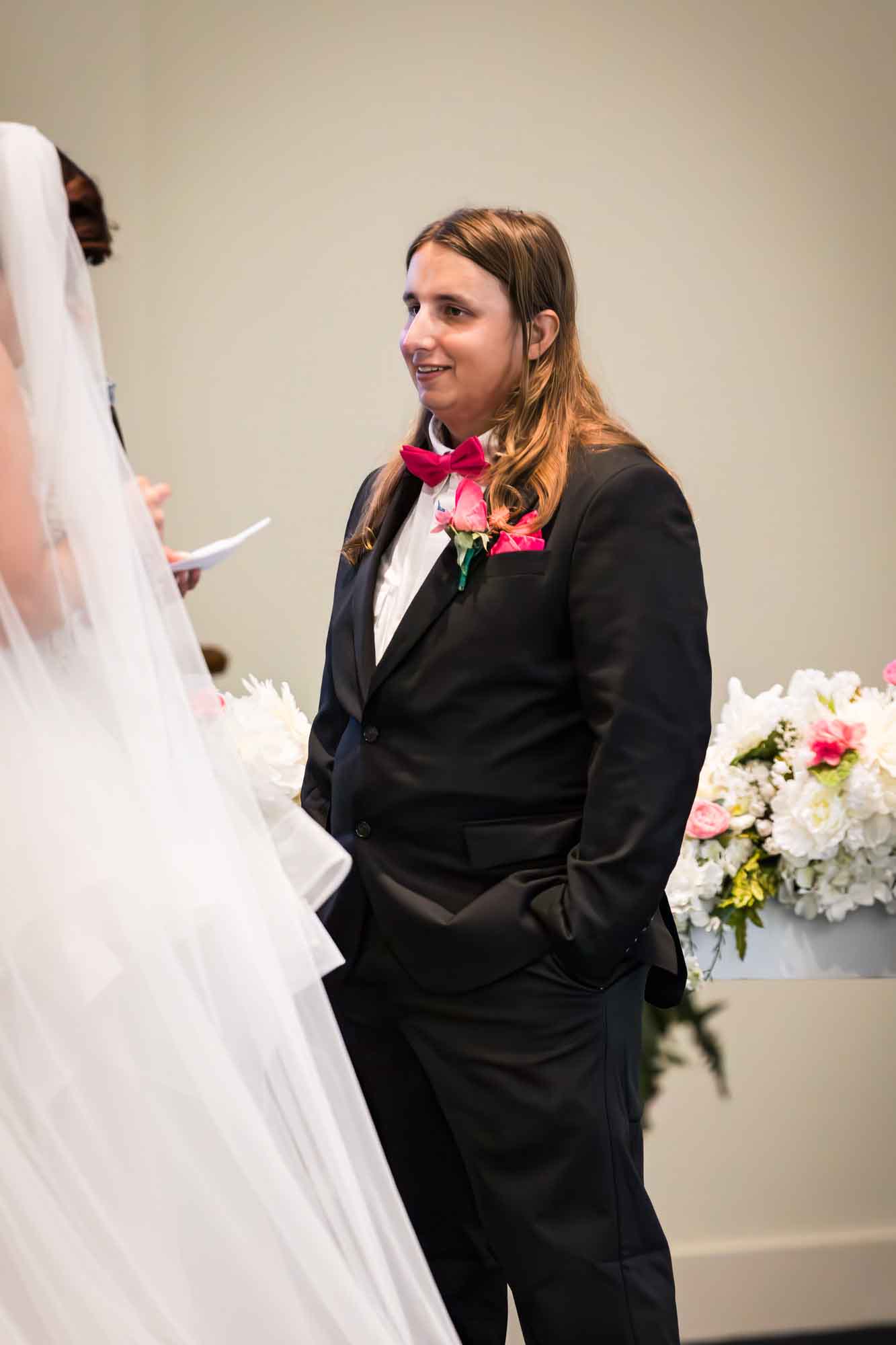 Cornerstone Church wedding photos of groom wearing black suit and pink bow tie standing in front of bride