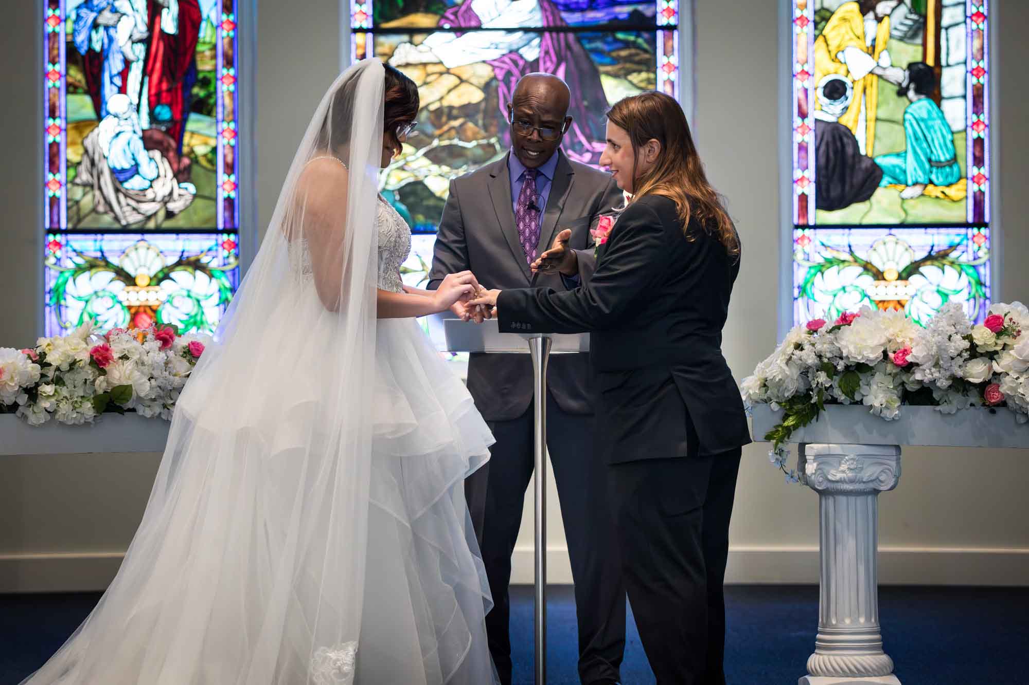 Cornerstone Church wedding photos of bride putting ring on groom's finger in front of African American officiant