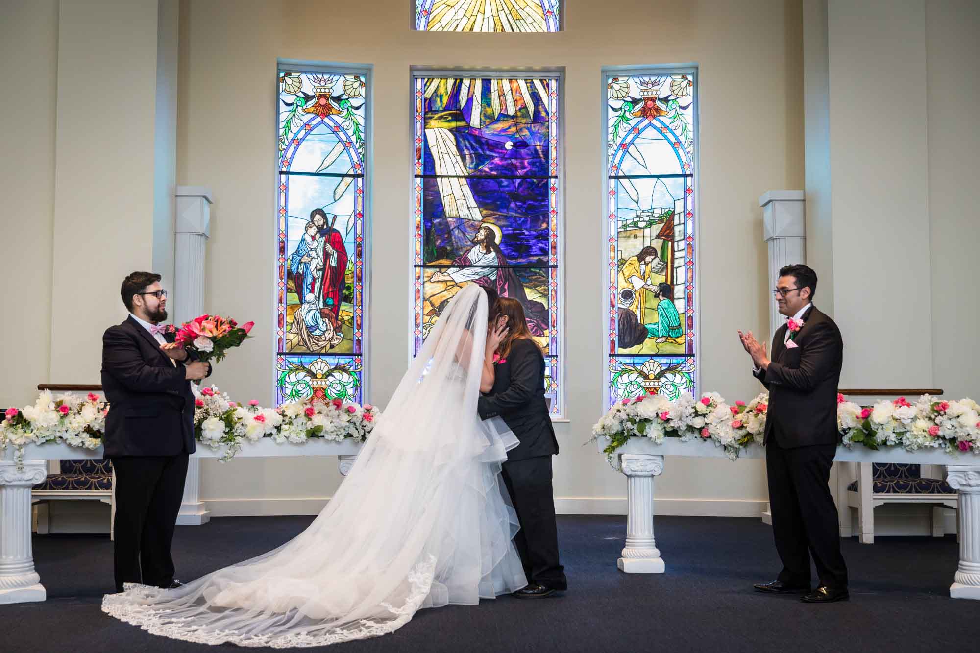 Cornerstone Church wedding photos of bride and groom kissing in front of stained glass windows with two groomsmen standing on either side
