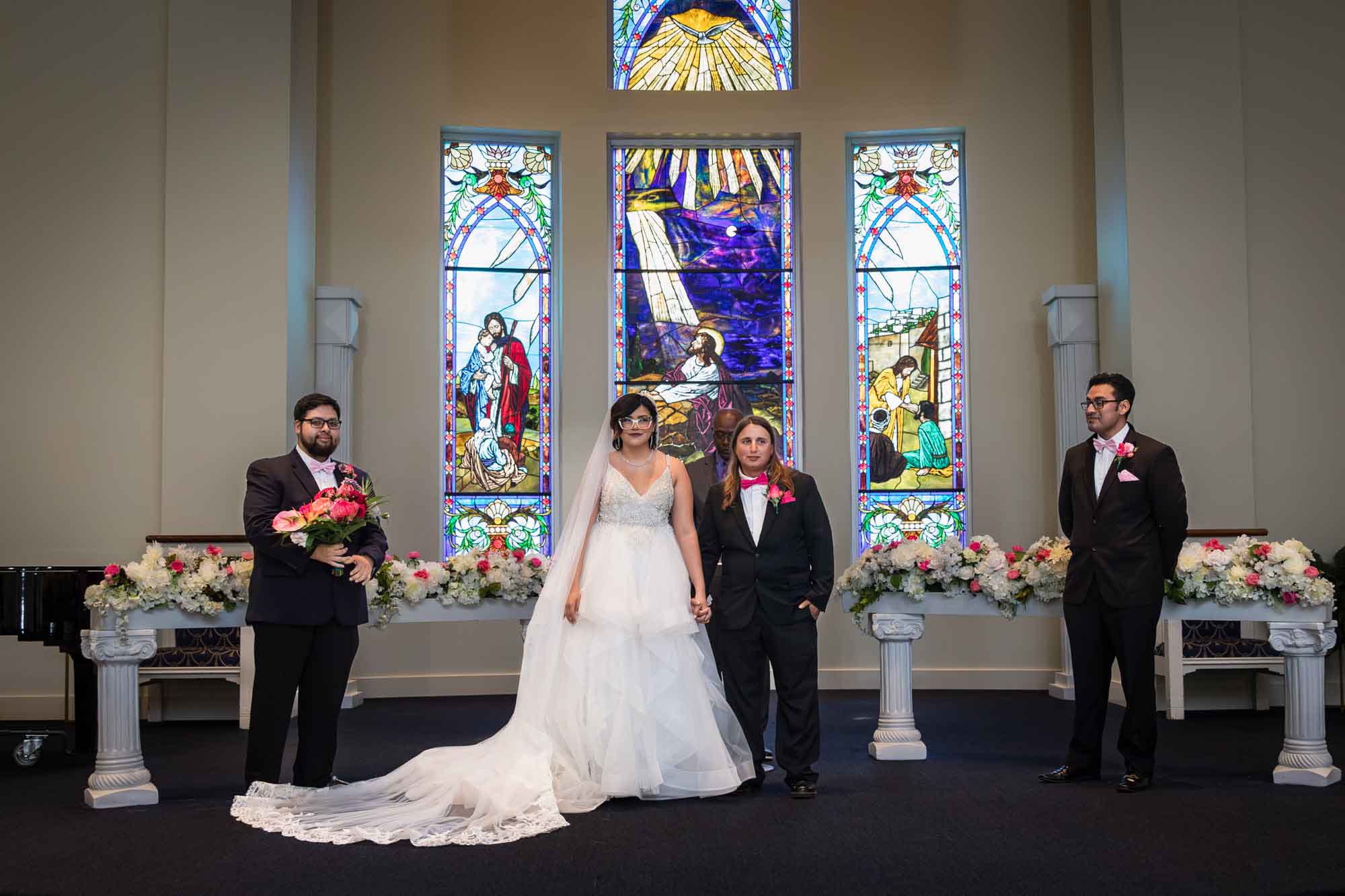 Cornerstone Church wedding photos of bride and groom standing in front of stained glass windows with two groomsmen in black suits standing on either side