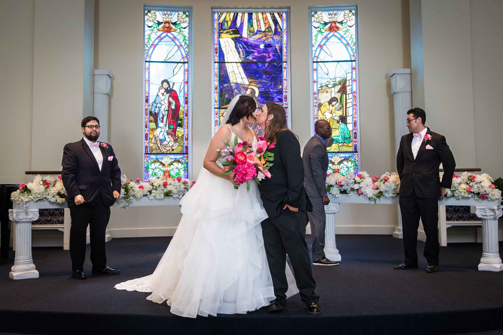 Cornerstone Church wedding photos of bride and groom kissing in front of bridal party and stained glass windows