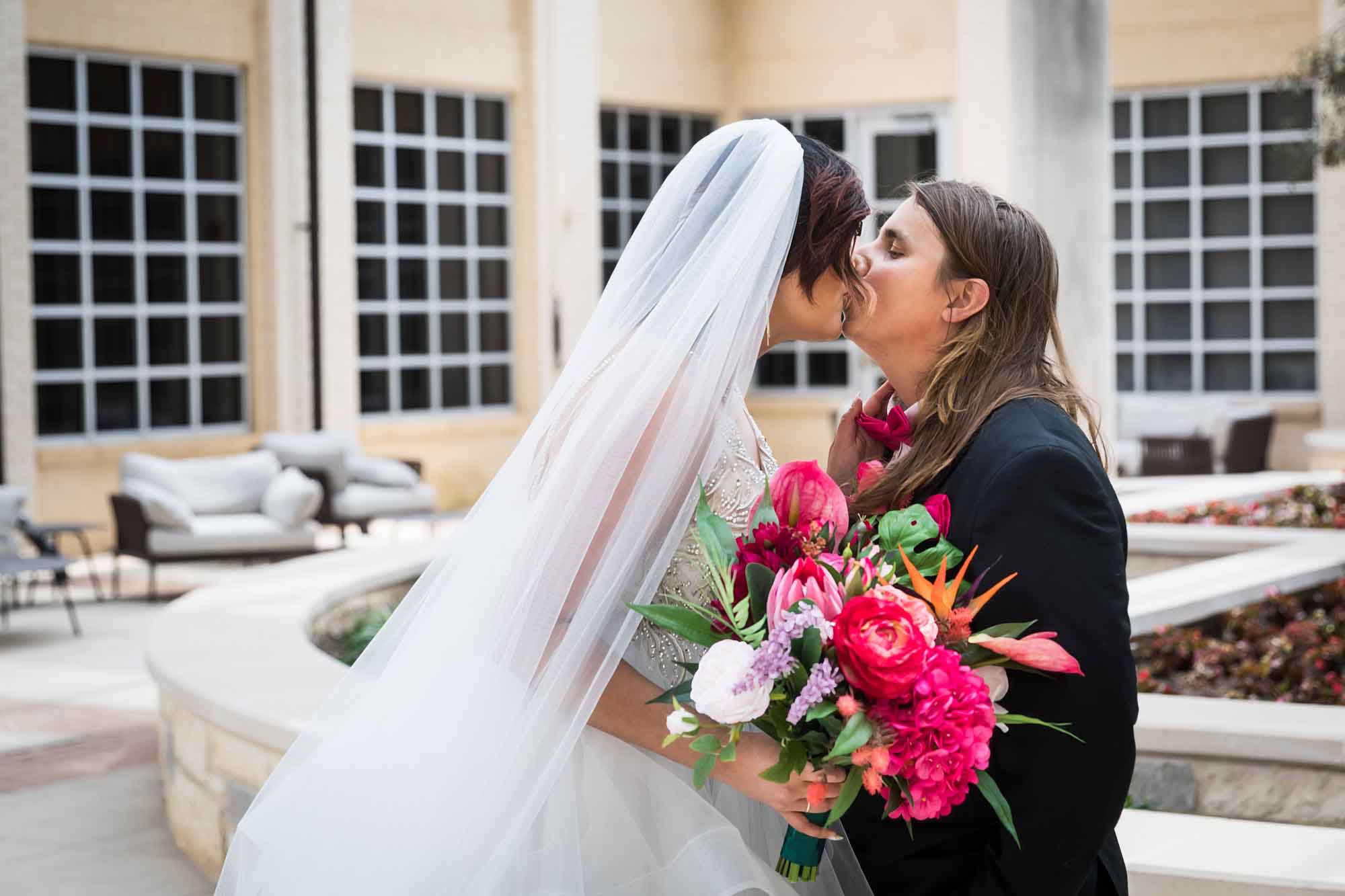 Cornerstone Church wedding photos of bride wearing veil and holding flower bouquet kissing groom wearing black suit