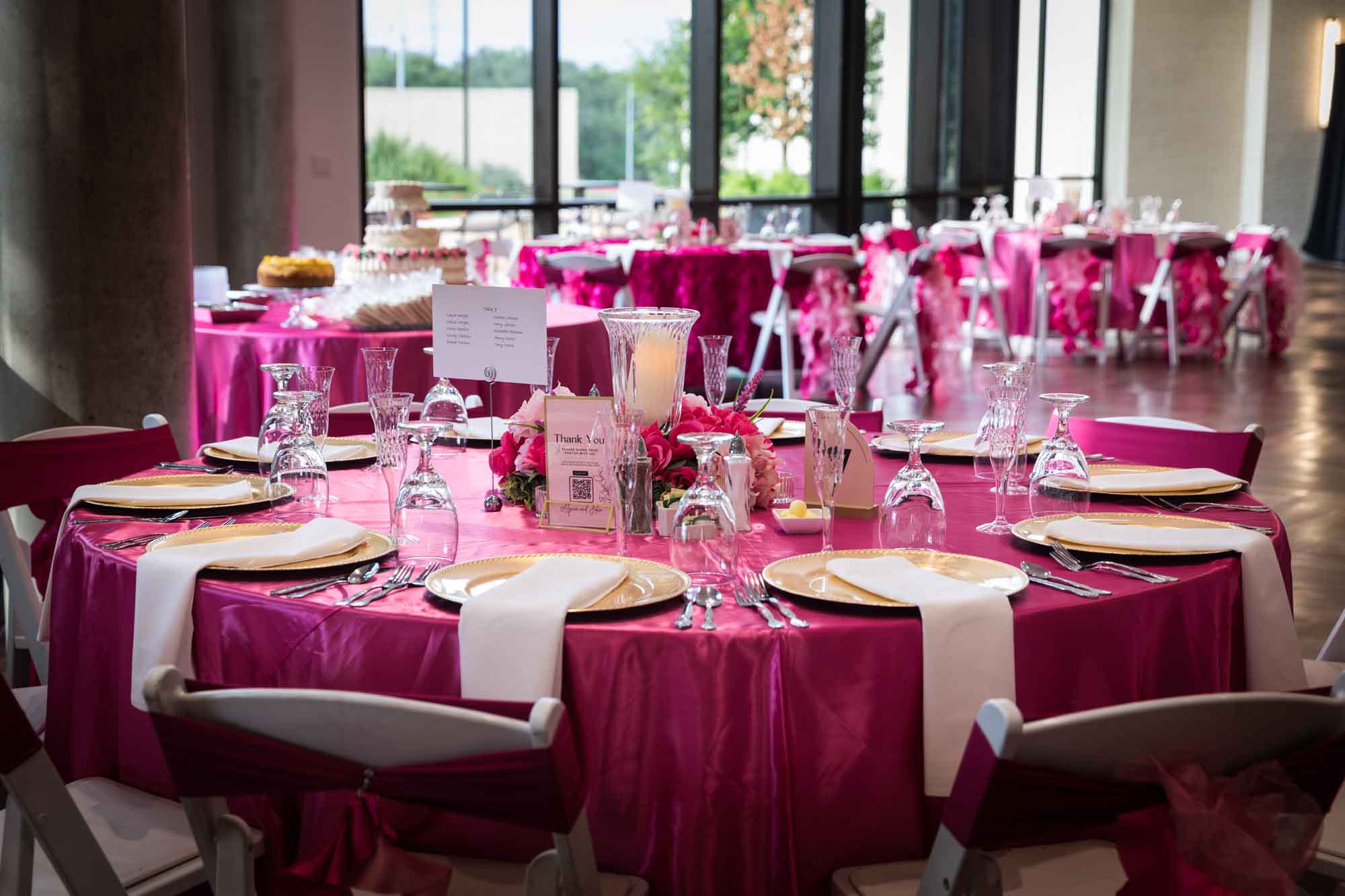 Wedding reception tables set with pink tablecloths, gold chargers, and glassware at Cornerstone Church