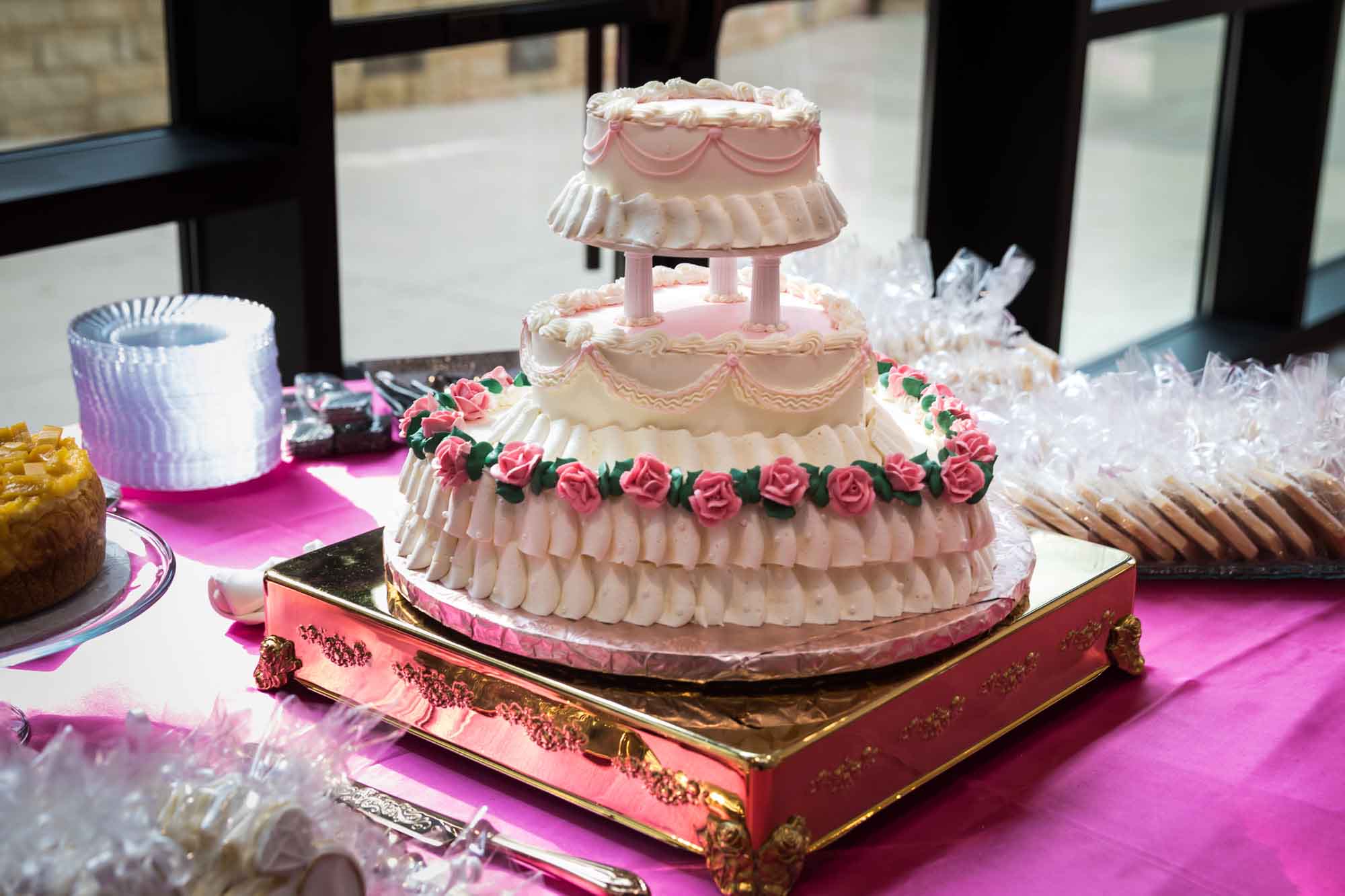 Three tiered wedding cake in the shape of a heart on a gold riser sitting on a pink tablecloth at Cornerstone Church