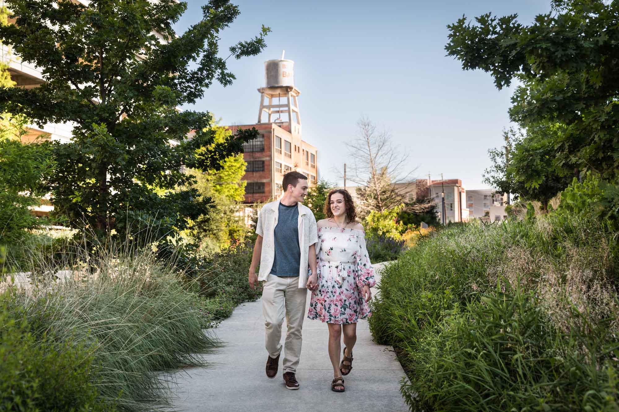 Downtown San Antonio engagement photos of couple walking in pathway in front of green bushes in San Pedro Creek Park