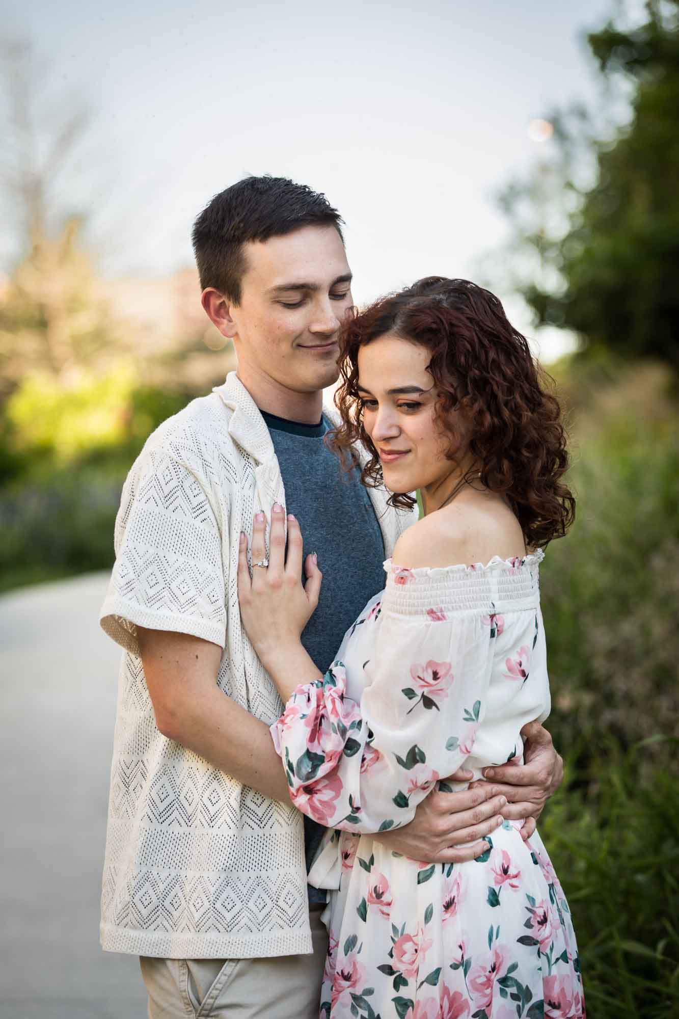 Downtown San Antonio engagement photos of couple hugging in middle of pathway in front of green bushes in San Pedro Creek Park