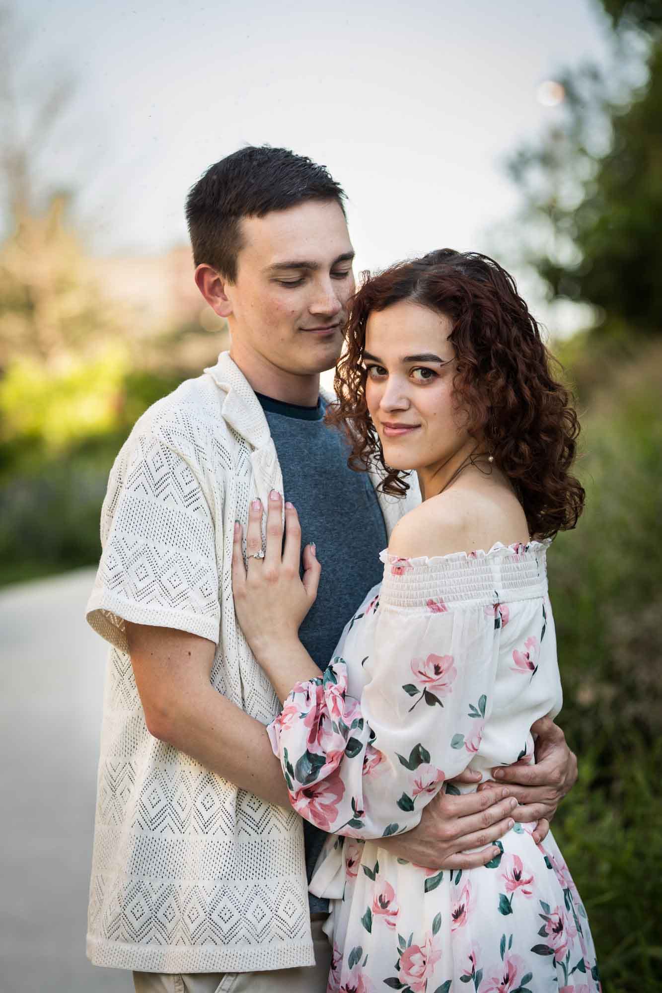 Downtown San Antonio engagement photos of couple hugging in middle of pathway in front of green bushes in San Pedro Creek Park