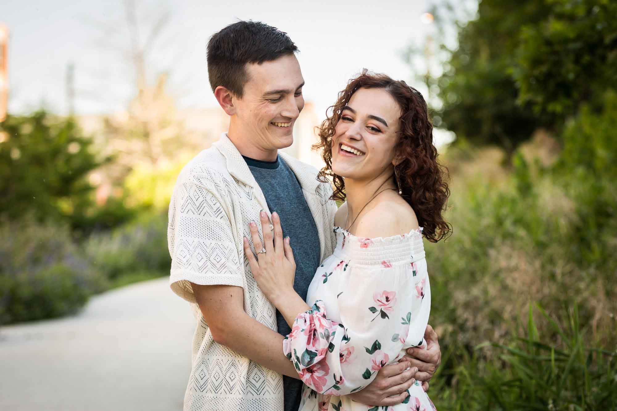 Downtown San Antonio engagement photos of couple hugging in middle of pathway in front of green bushes in San Pedro Creek Park