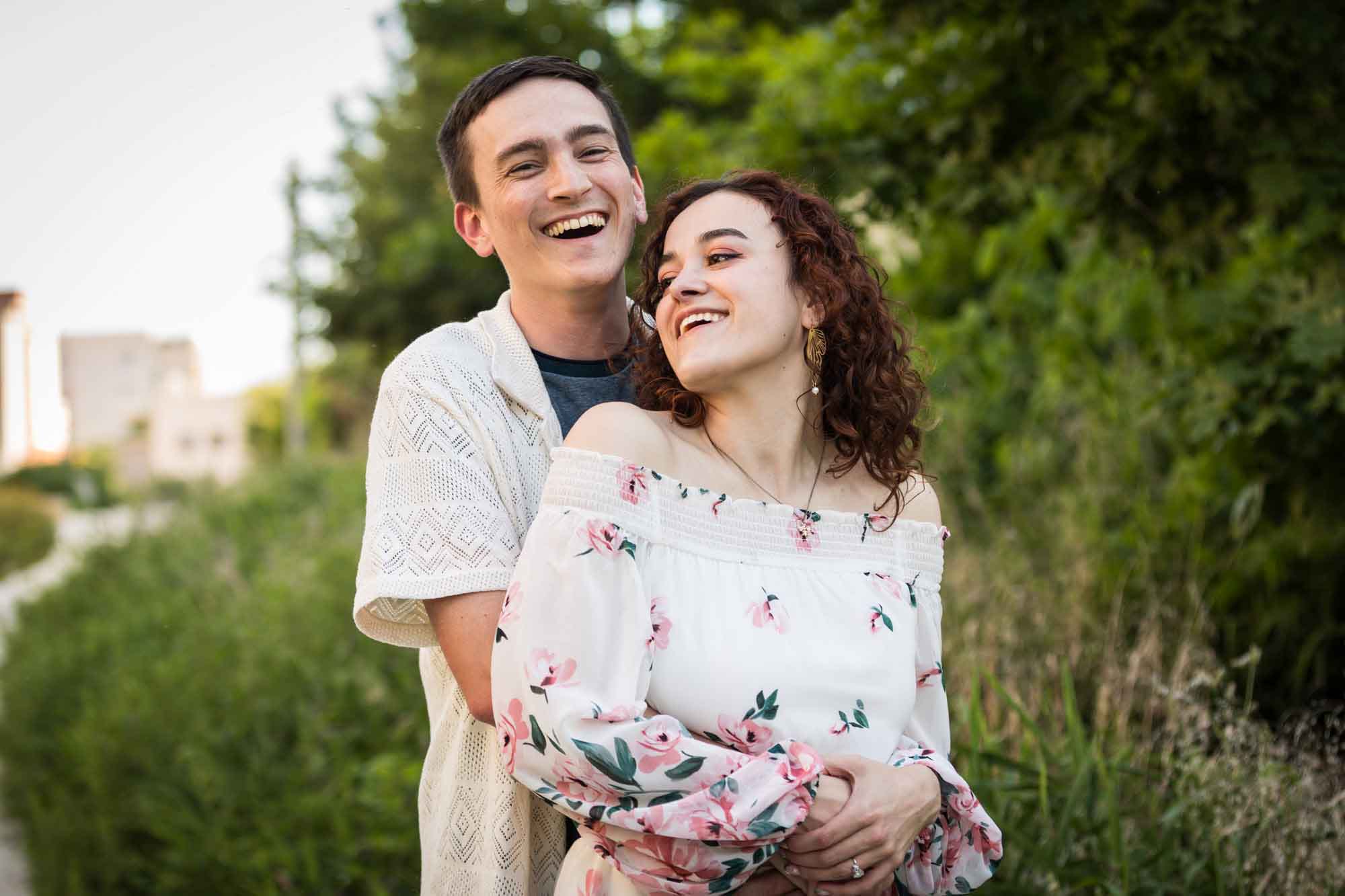 Downtown San Antonio engagement photos of couple hugging in front of green bushes in San Pedro Creek Park