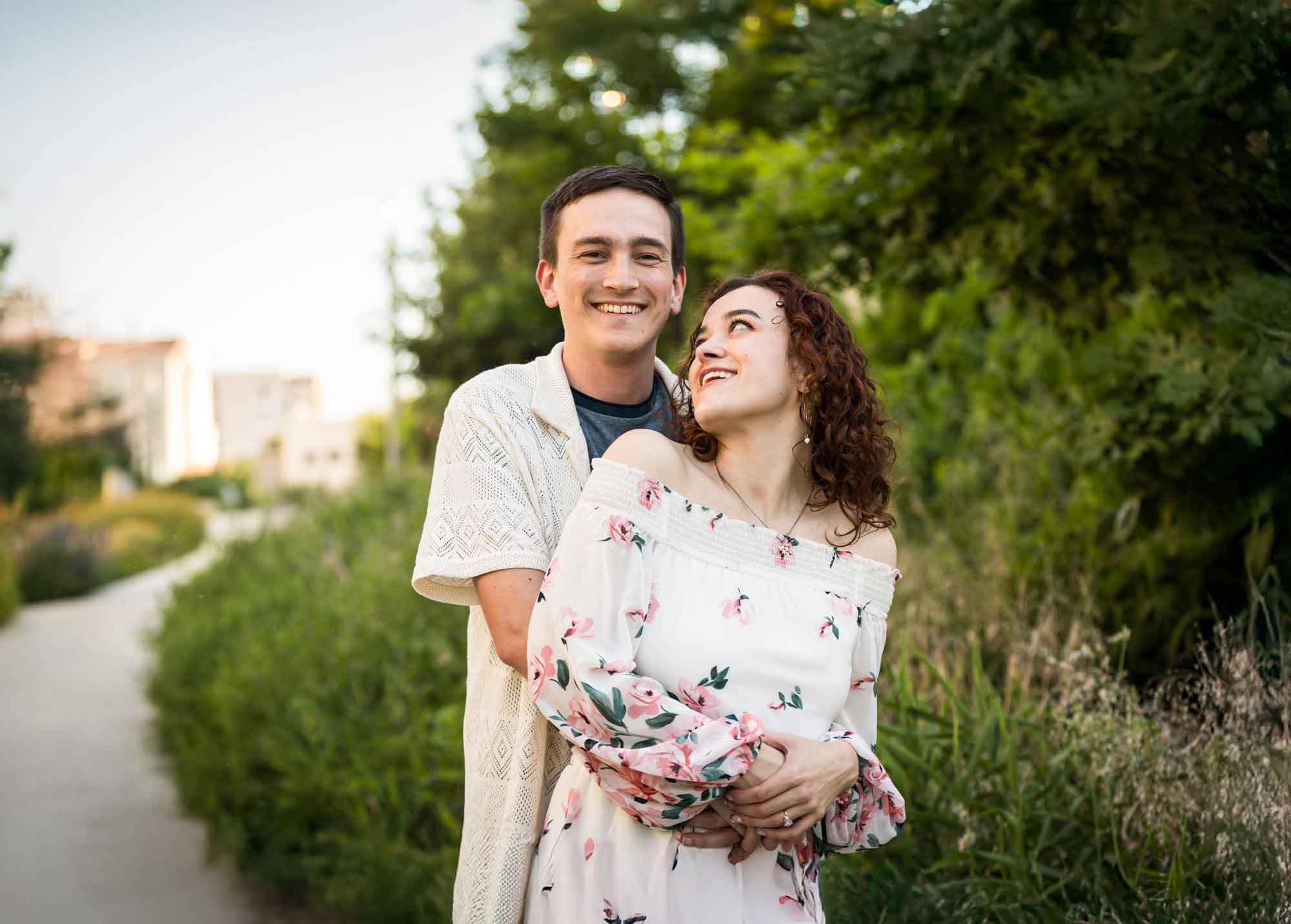 Downtown San Antonio engagement photos of couple hugging in front of green bushes in San Pedro Creek Park