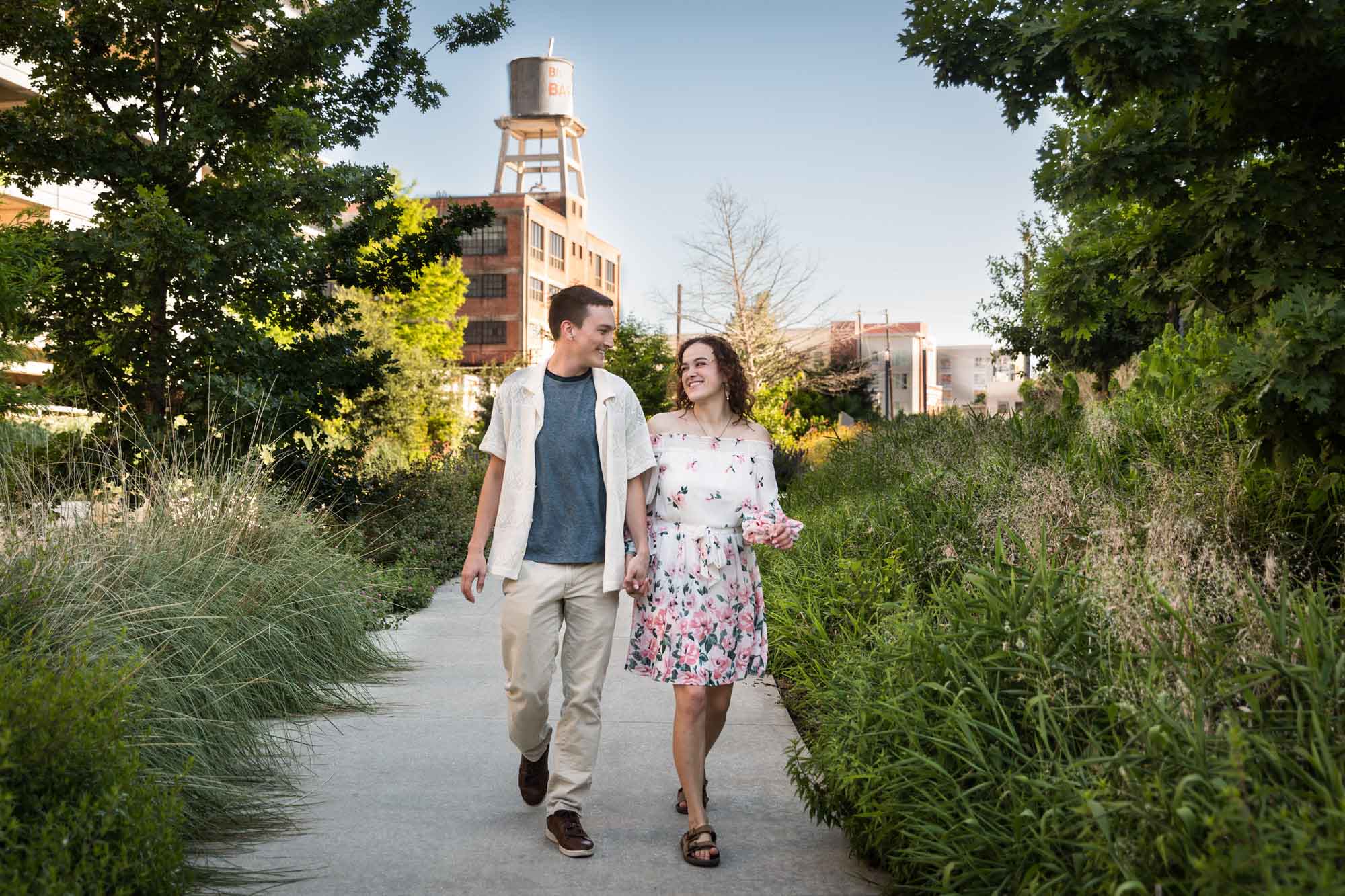 Downtown San Antonio engagement photos of couple walking in pathway in front of green bushes in San Pedro Creek Park