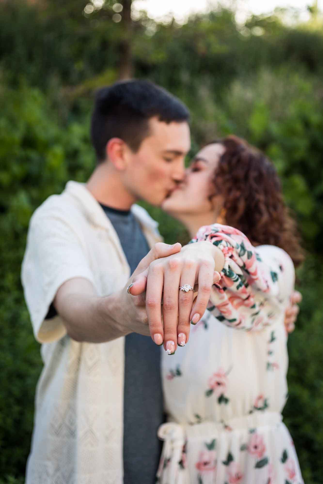 Downtown San Antonio engagement photos of couple showing off engagement ring on woman's hand while kissing in San Pedro Creek Park