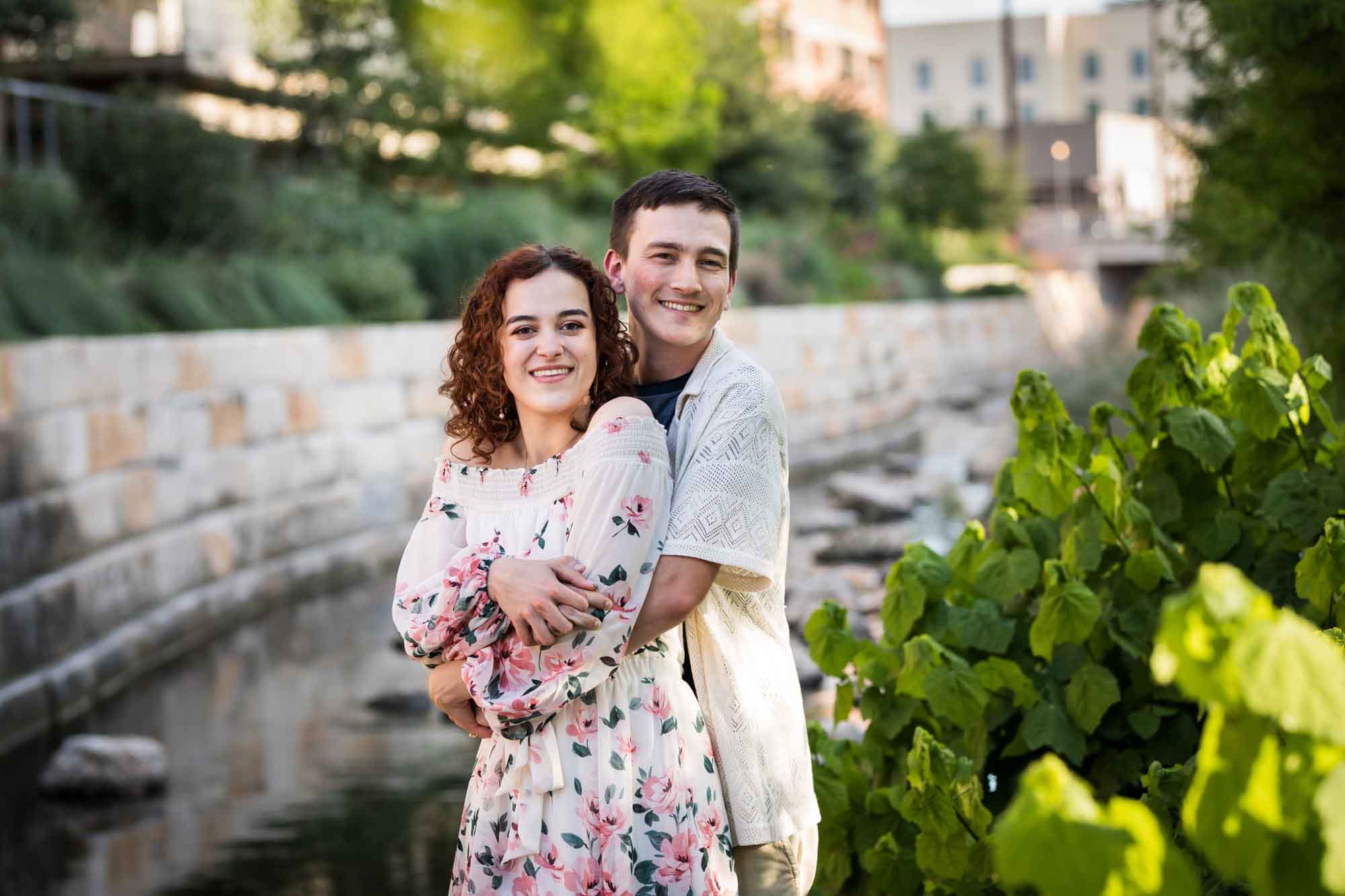 Downtown San Antonio engagement photos of couple hugging in front of brick wall in San Pedro Creek Park