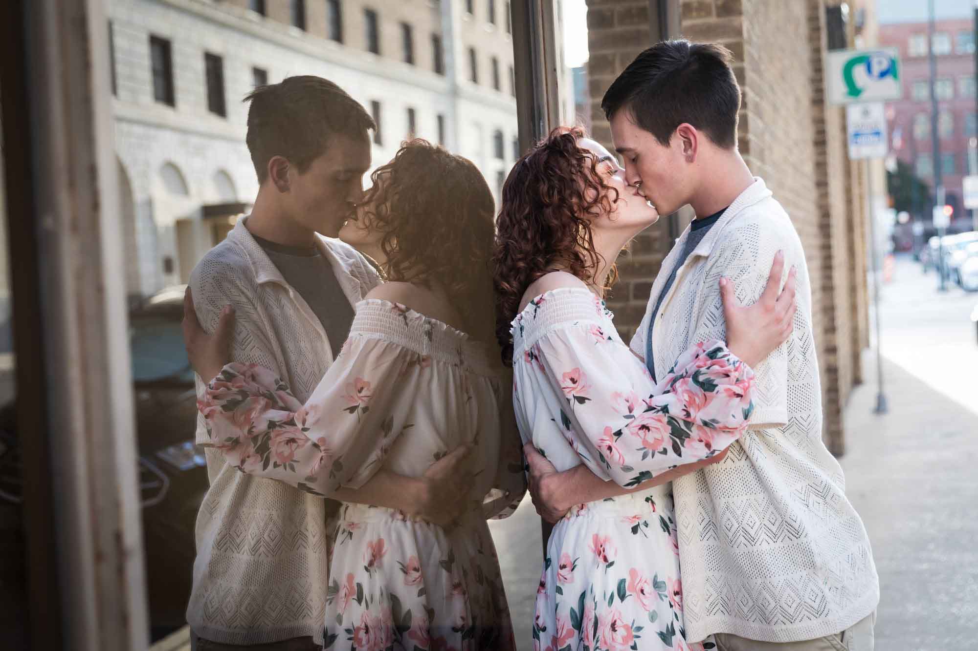Downtown San Antonio engagement photos of couple on sidewalk leaning against window with reflection