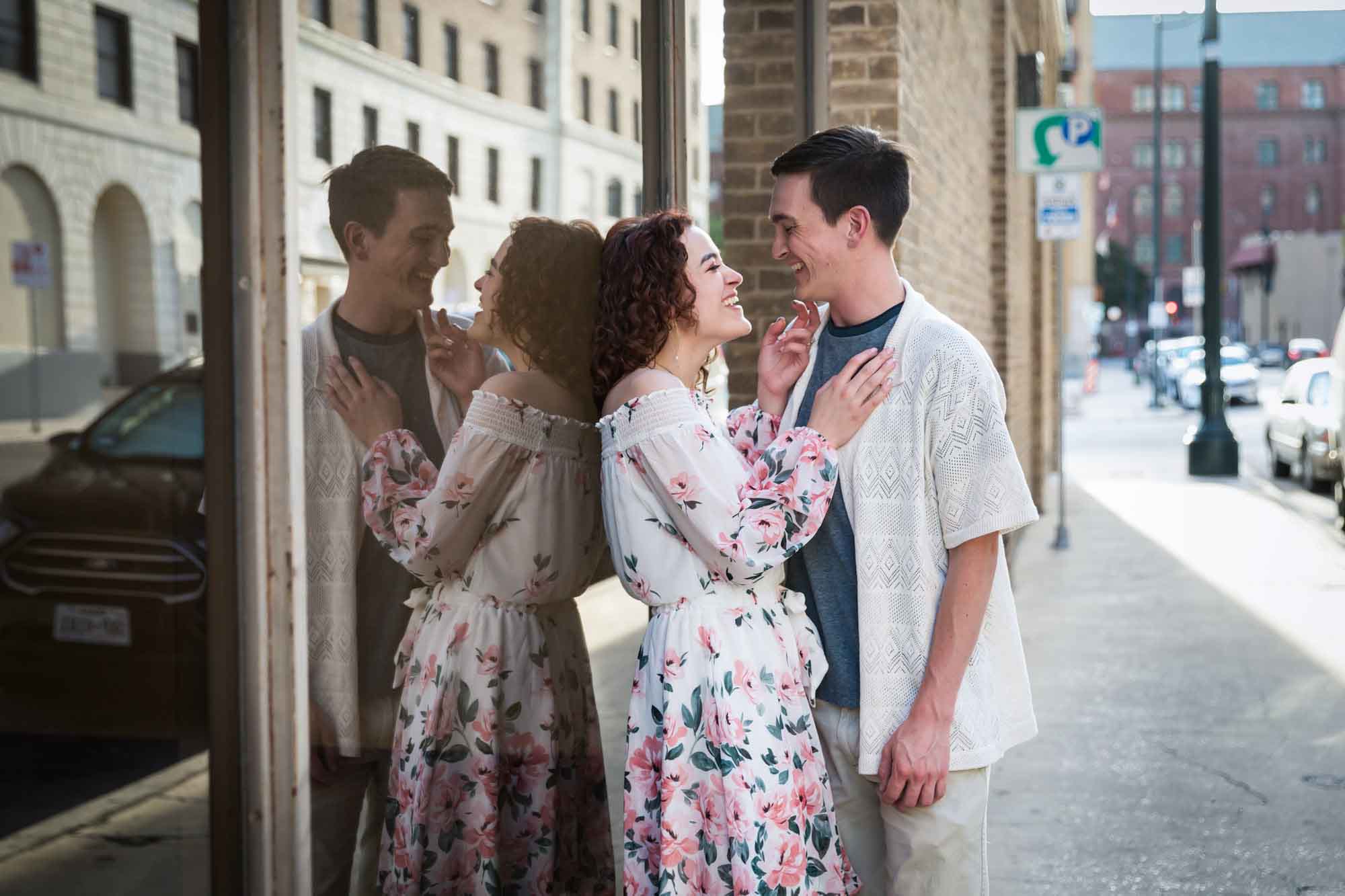 Downtown San Antonio engagement photos of couple on sidewalk leaning against window with reflection