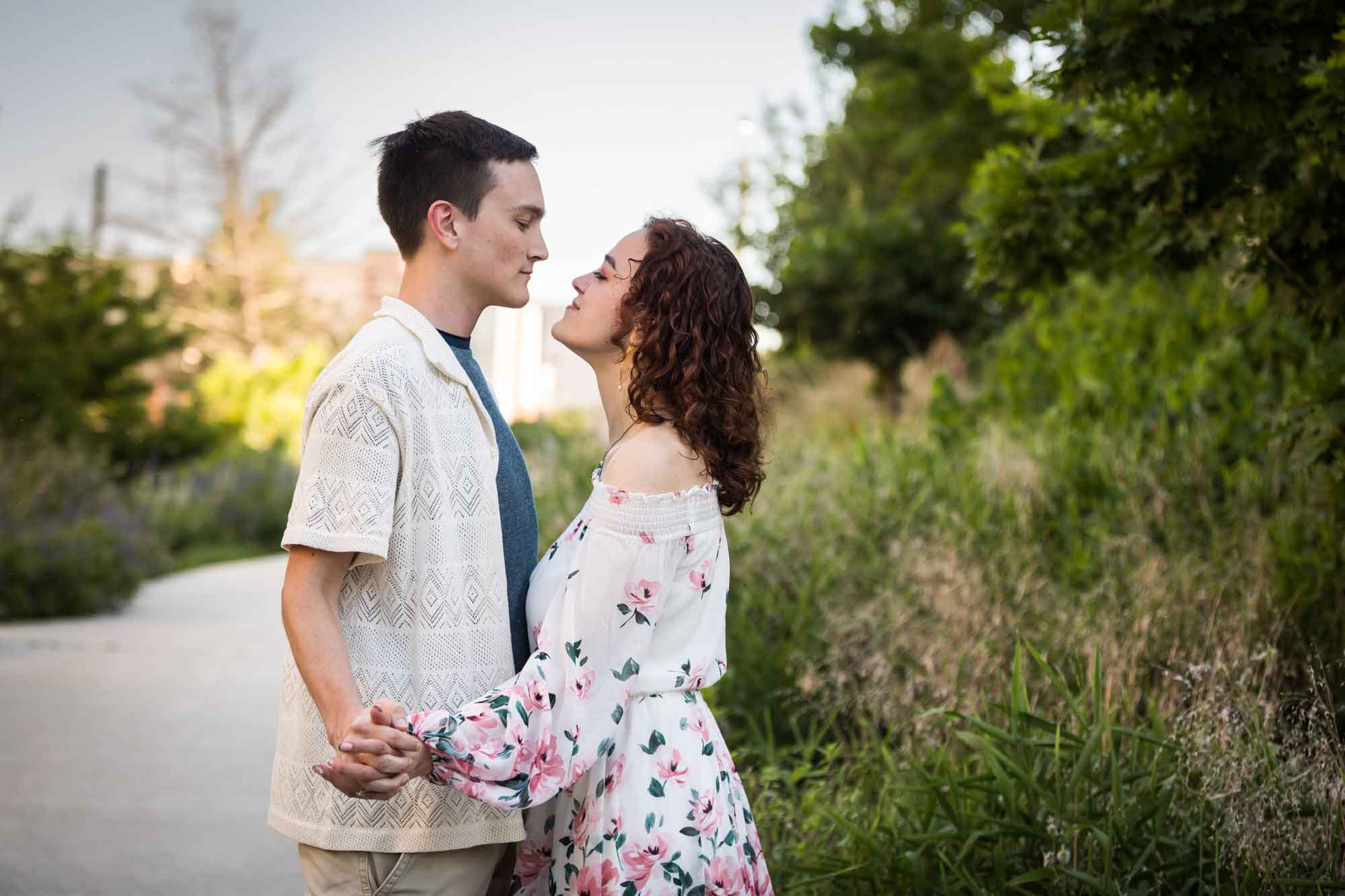 Downtown San Antonio engagement photos of couple hugging in middle of pathway in front of green bushes in San Pedro Creek Park