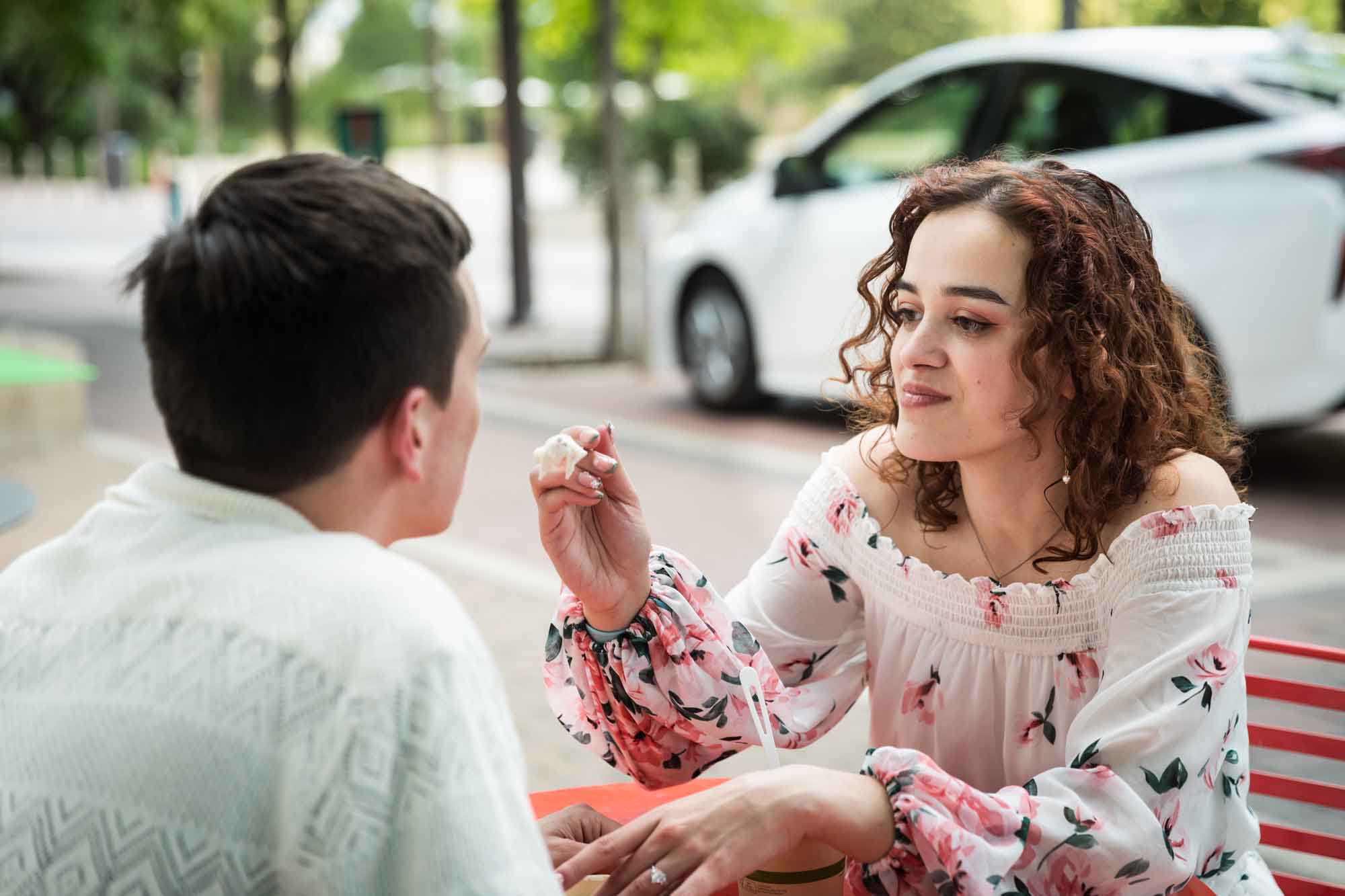 Woman feeding man ice cream with a spoon during a downtown San Antonio engagement portrait session