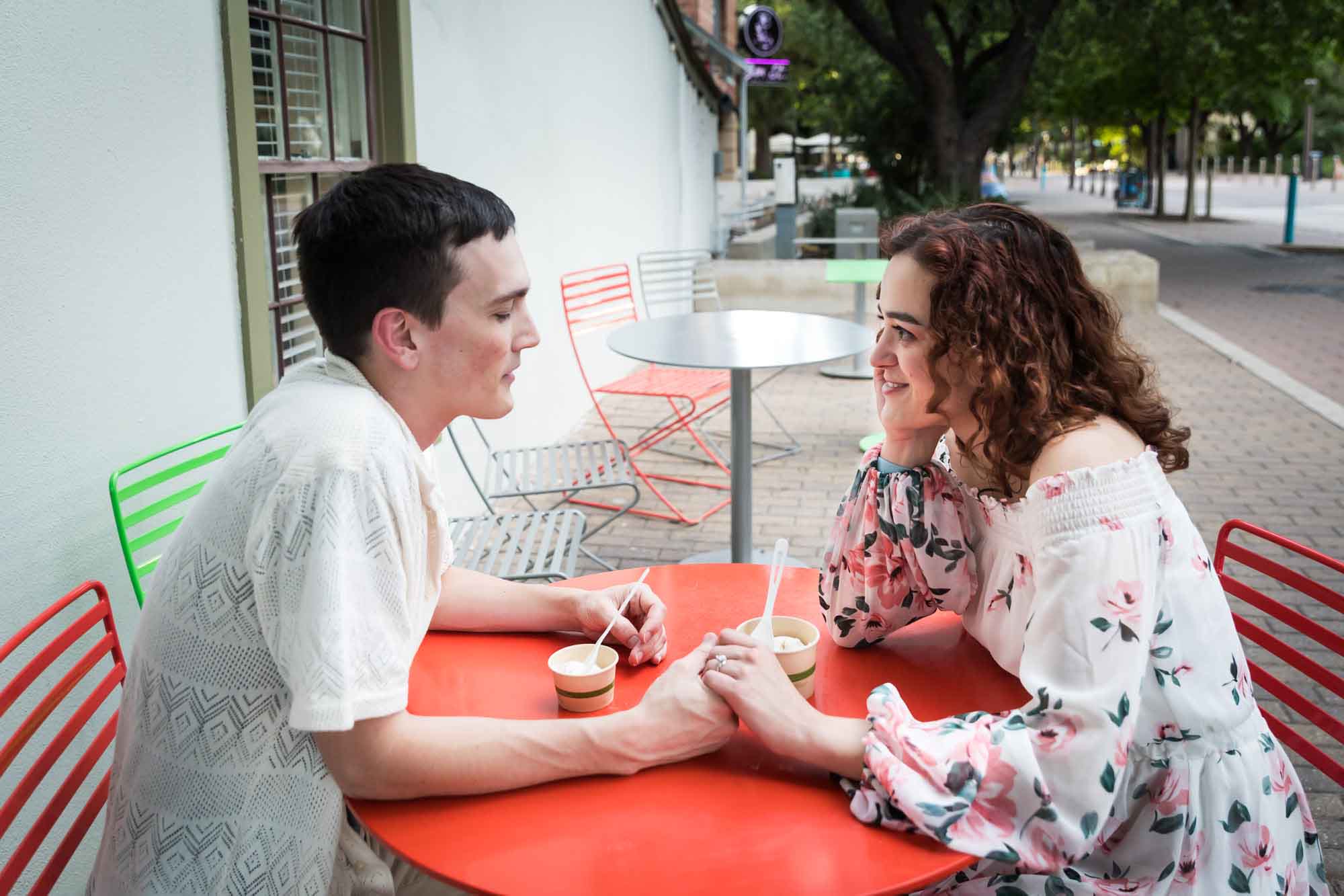 Close up of couple eating ice cream and holding hands at red table during a downtown San Antonio engagement portrait session