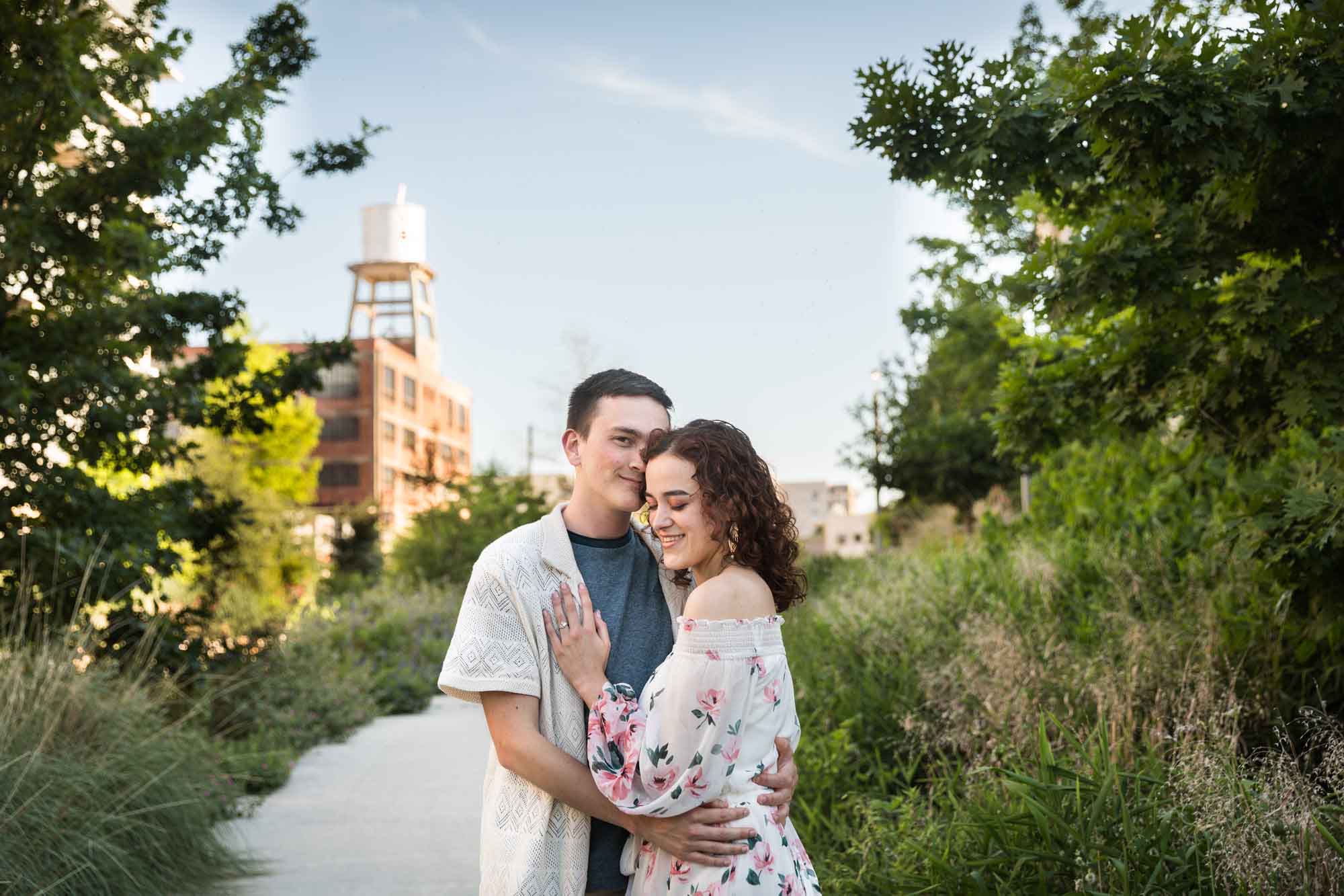 Downtown San Antonio engagement photos of couple hugging in middle of pathway in front of green bushes in San Pedro Creek Park