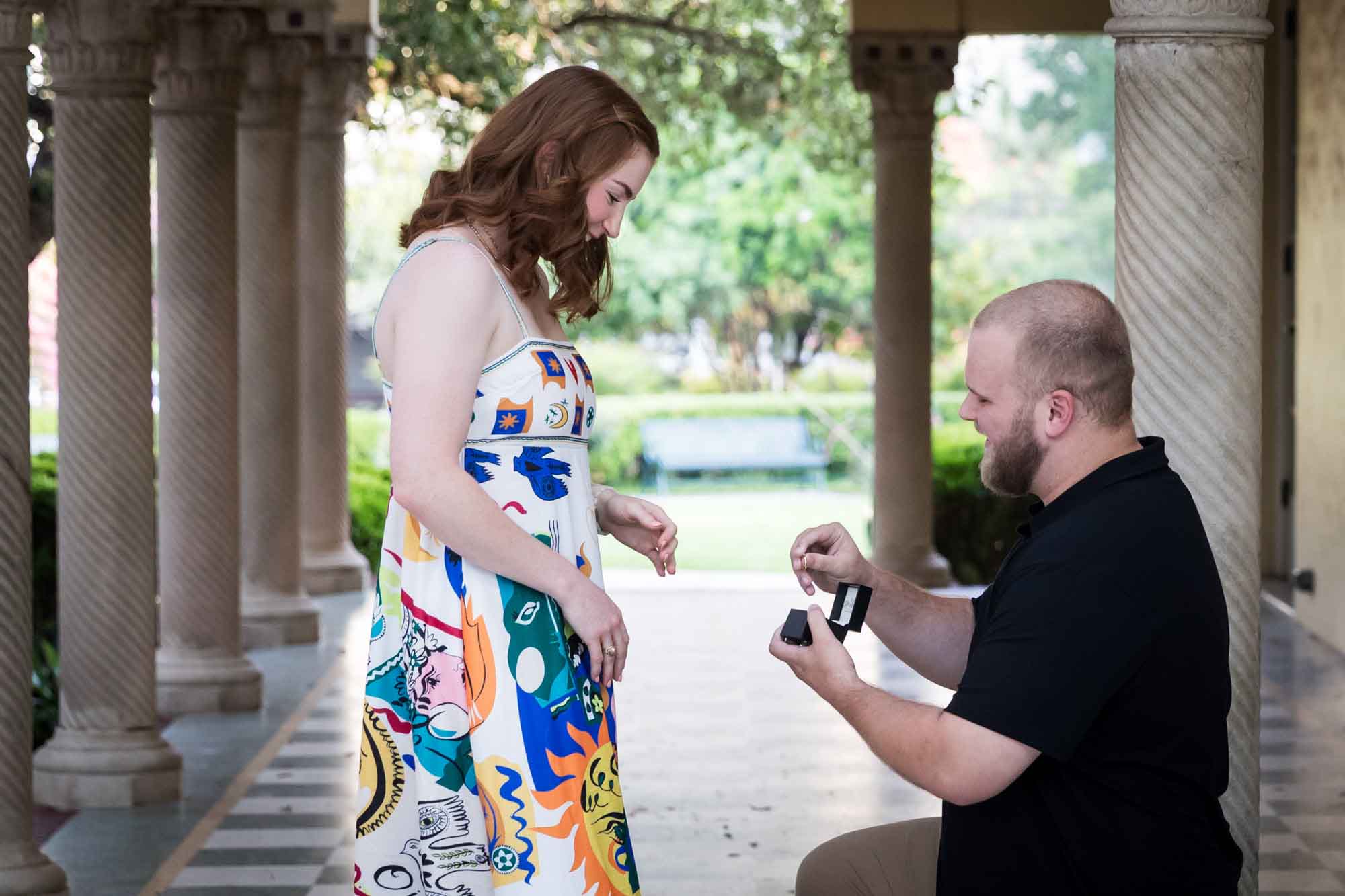 Man down on one knee proposing to a woman in front of colonnade for an article on how to propose at the Landa Library