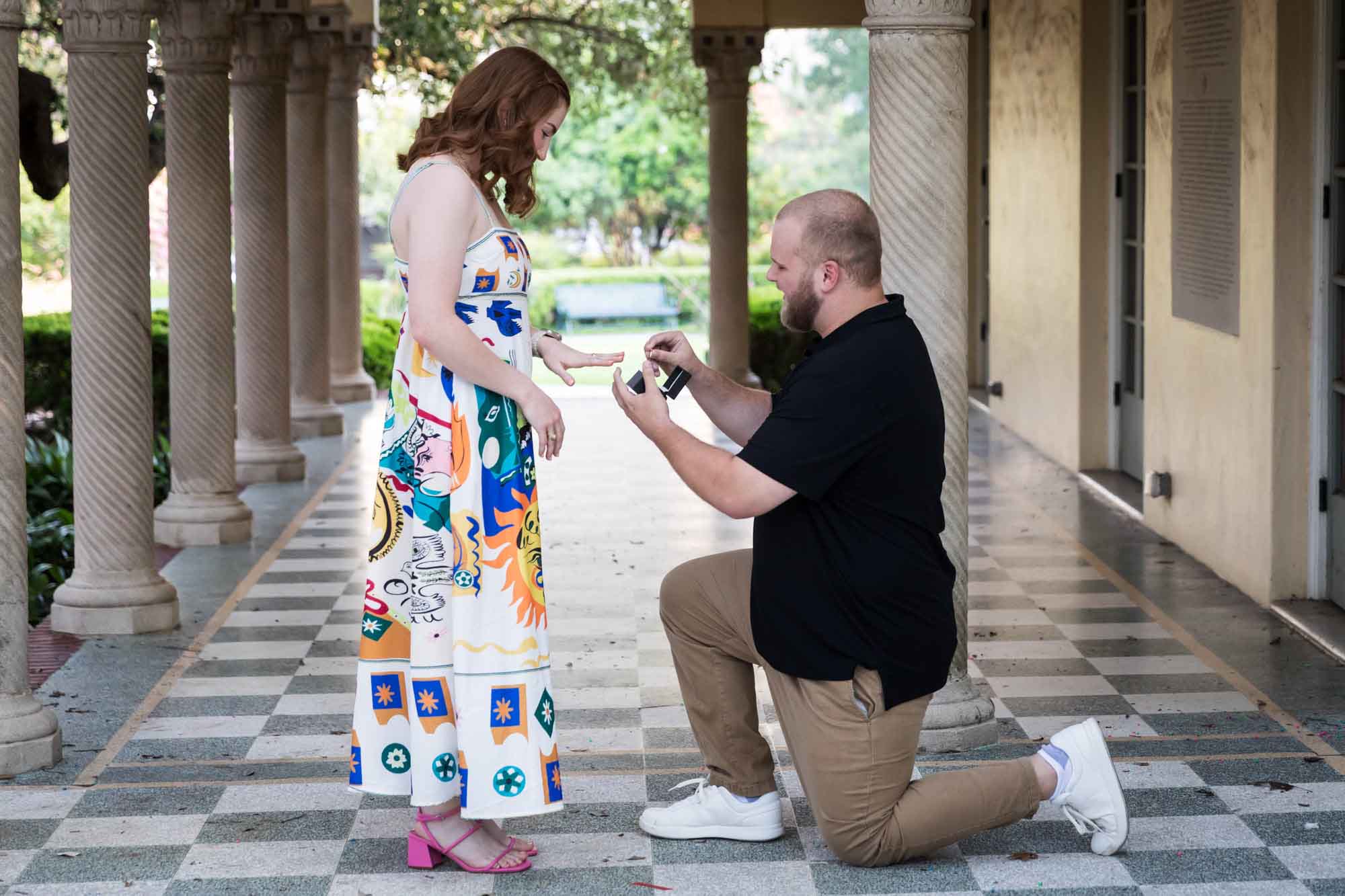 Man down on one knee proposing to a woman in front of colonnade for an article on how to propose at the Landa Library