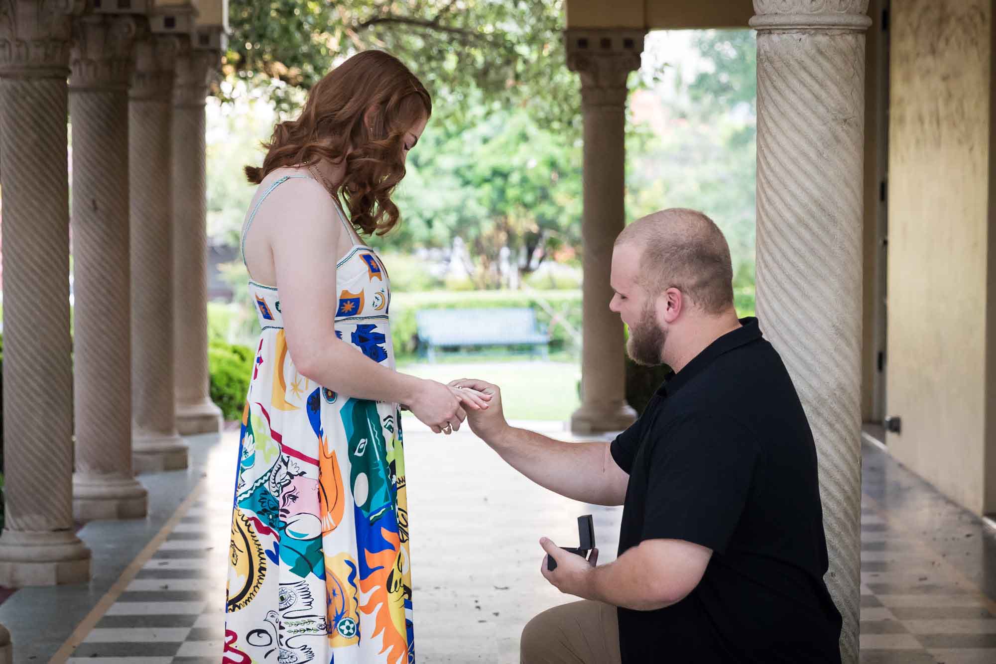 Man down on one knee proposing to a woman in front of colonnade for an article on how to propose at the Landa Library