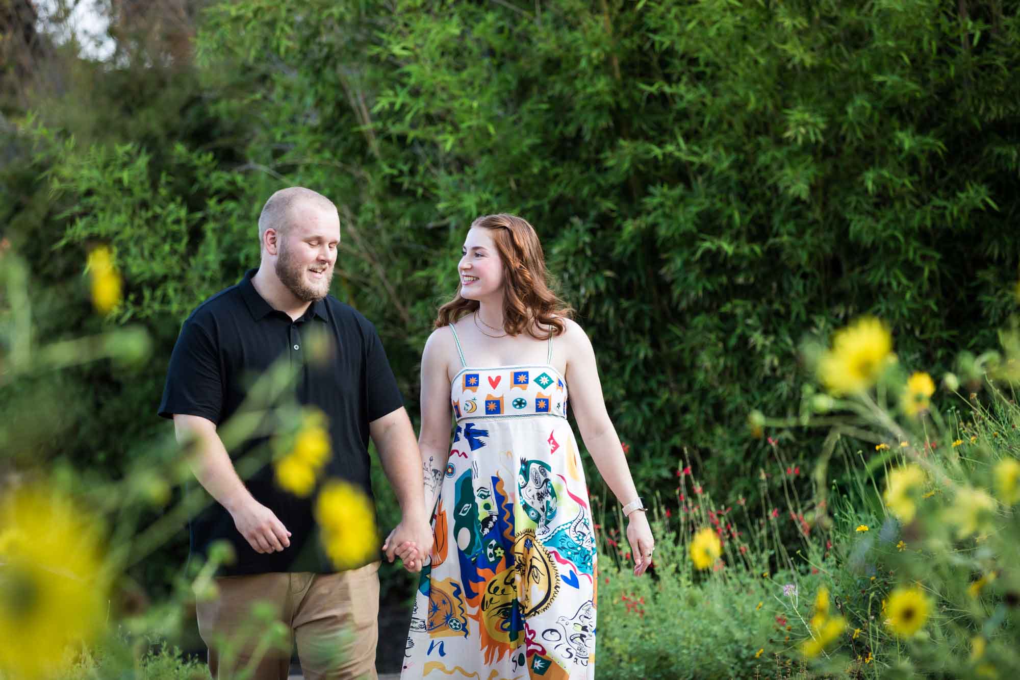 Couple holding hands walking through flower garden during a Landa Library engagement portrait