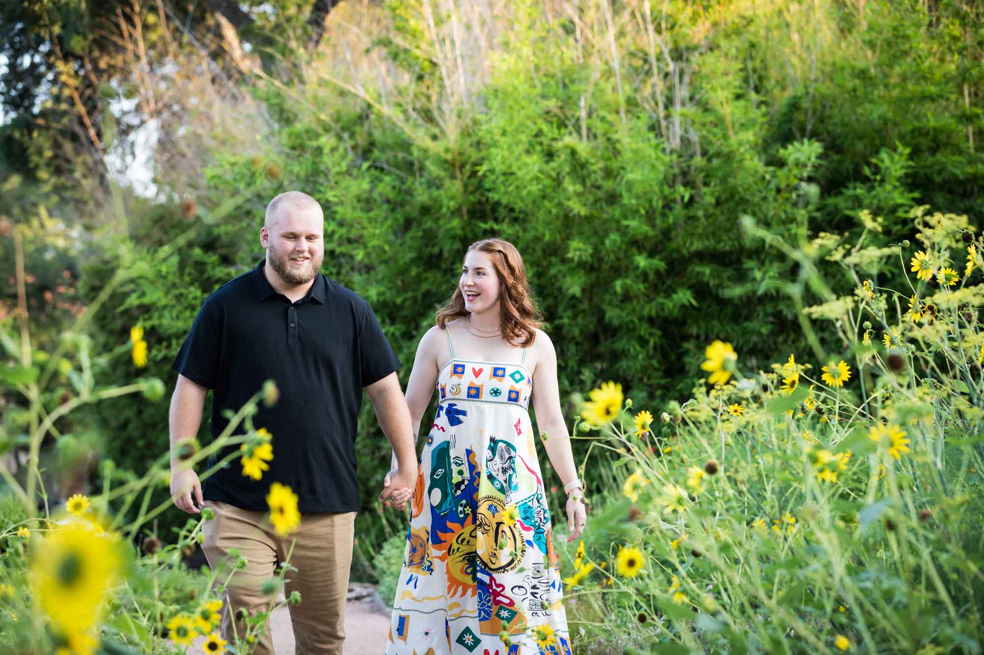 Couple holding hands walking through flower garden during a Landa Library engagement portrait
