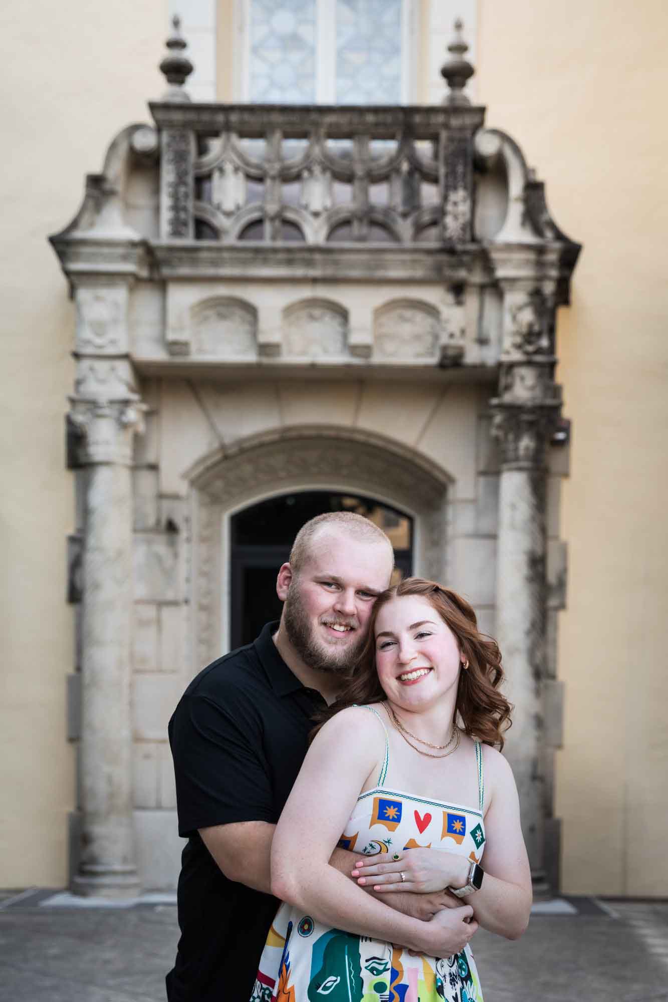 Couple hugging in front of Landa Library main building facade for an article on how to propose at the Landa Library