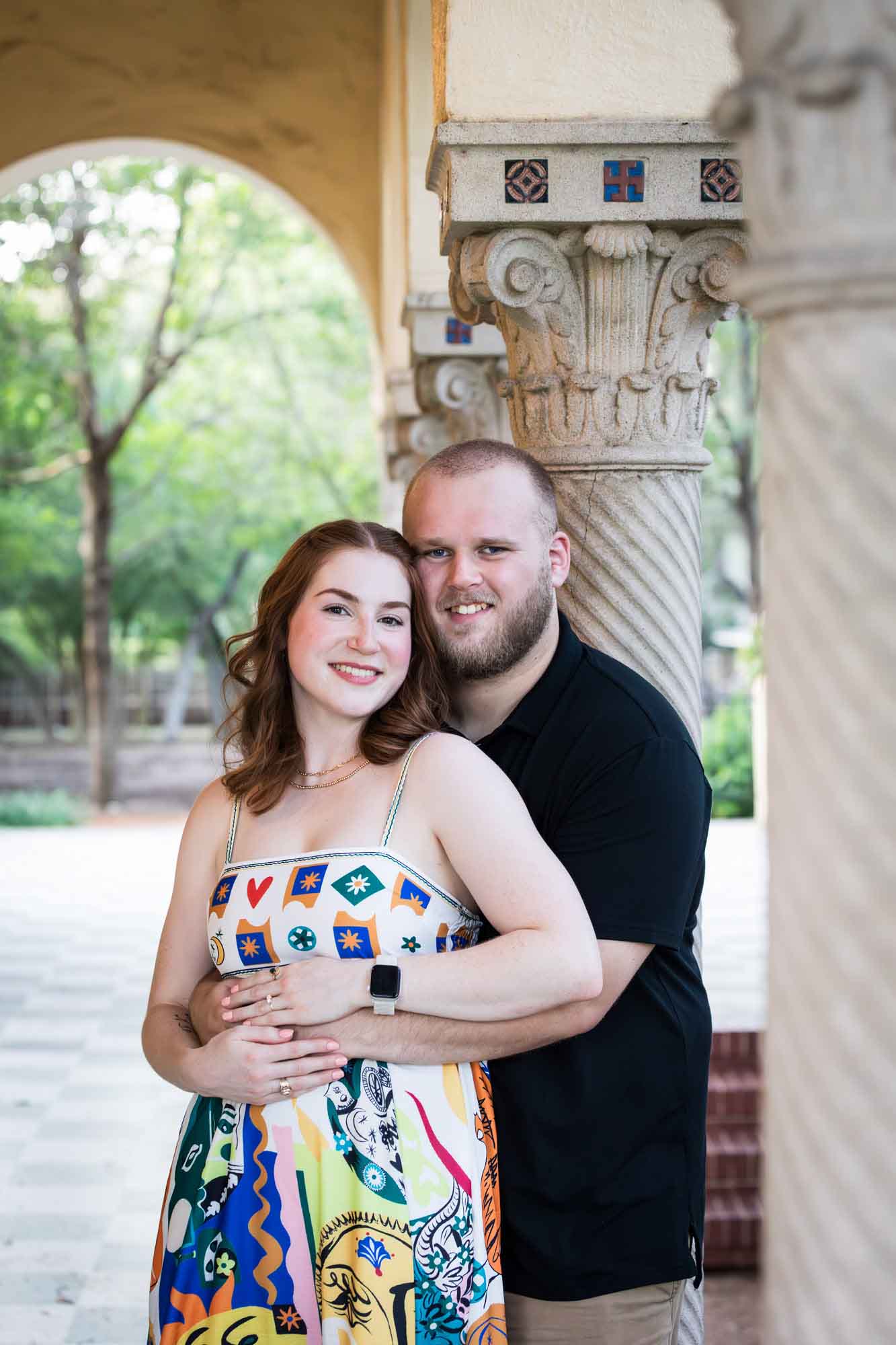 Couple hugging beside concrete column for an article on how to propose at the Landa Library