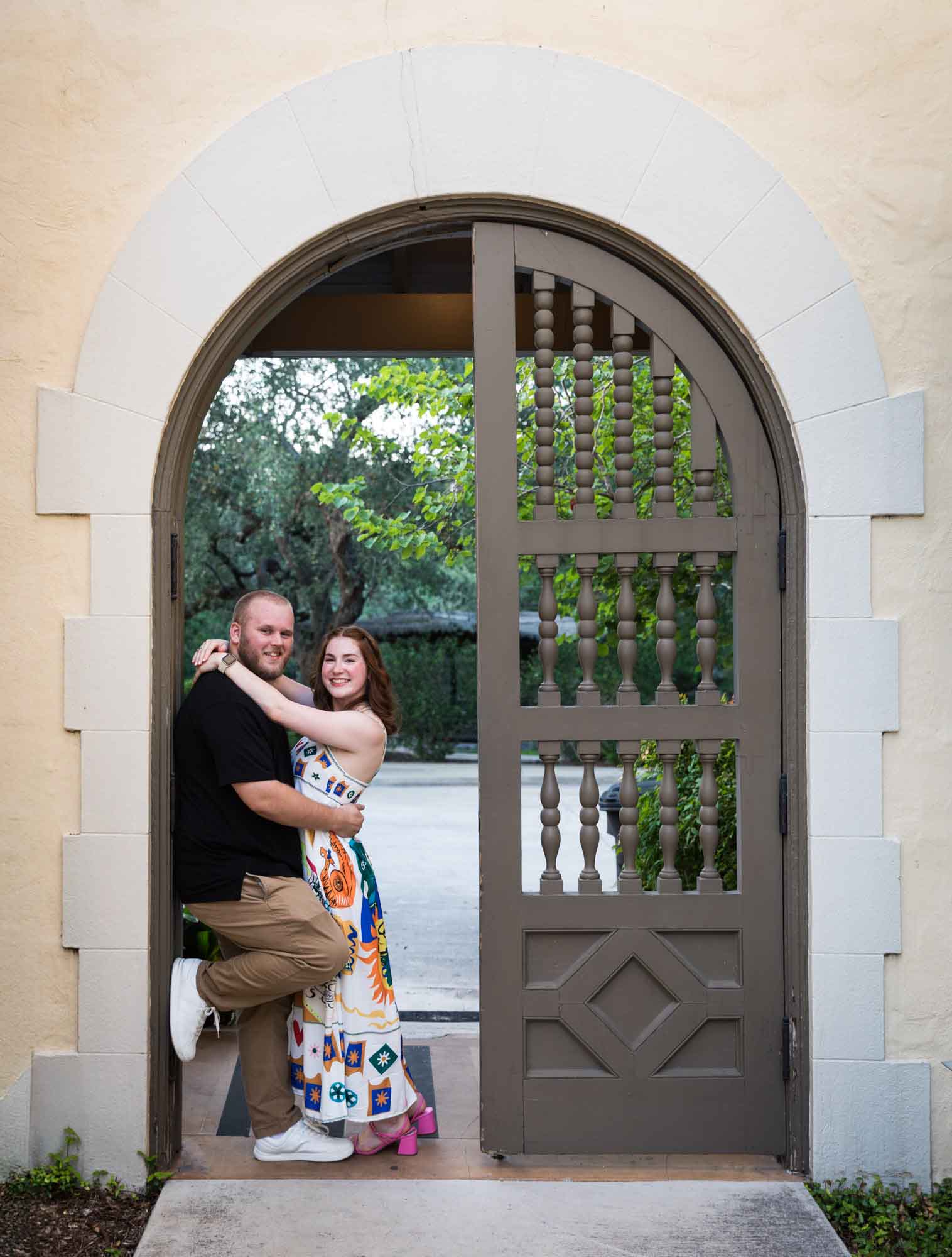 Couple hugging beside wooden gate for an article on how to propose at the Landa Library