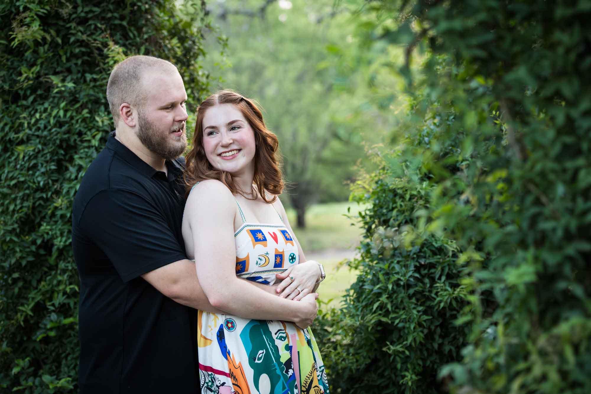 Couple hugging in front of vine-covered trees during a Landa Library engagement portrait