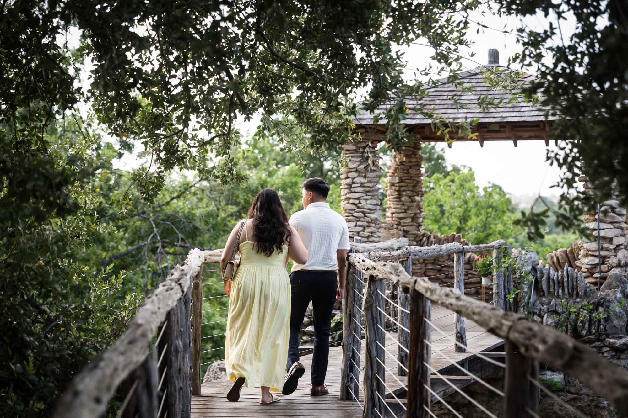 Man and woman wearing yellow dress walking on wooden pathway towards stone gazebo