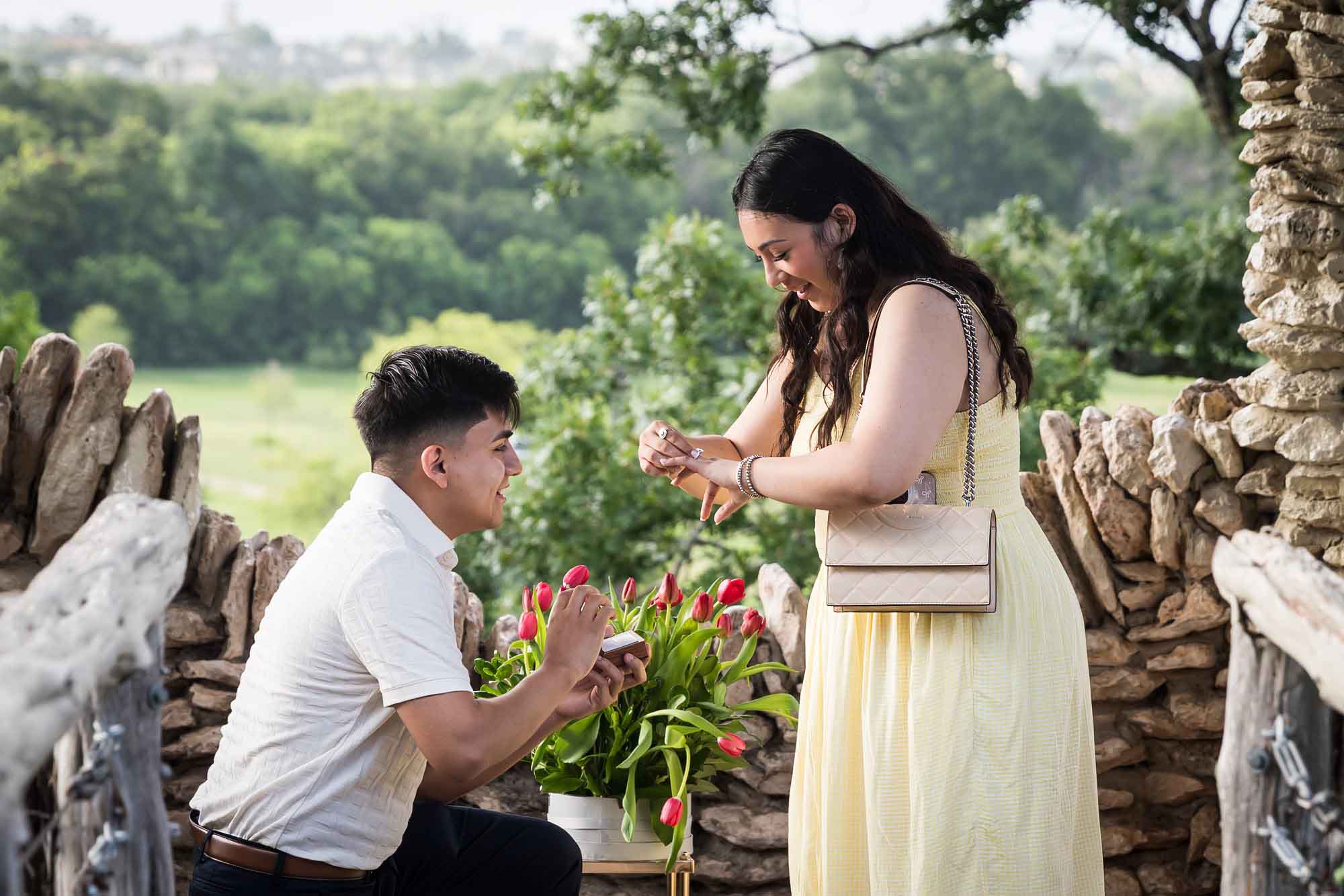 Man wearing black pants bending down on one knee in front of woman wearing yellow dress in stone gazebo during proposal for an article on Japanese Tea Garden proposal tips