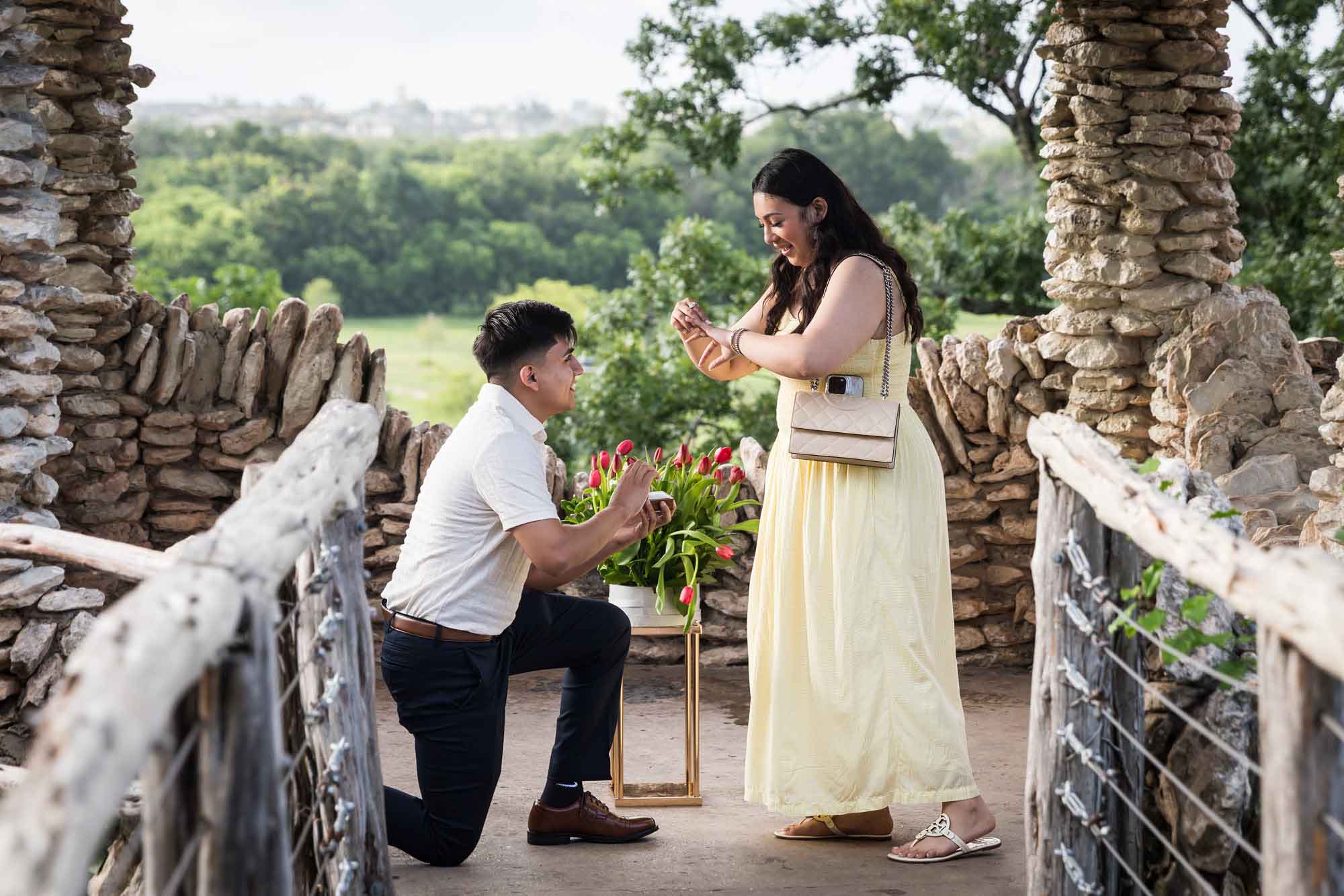 Man wearing black pants bending down on one knee in front of woman wearing yellow dress in stone gazebo during proposal for an article on Japanese Tea Garden proposal tips