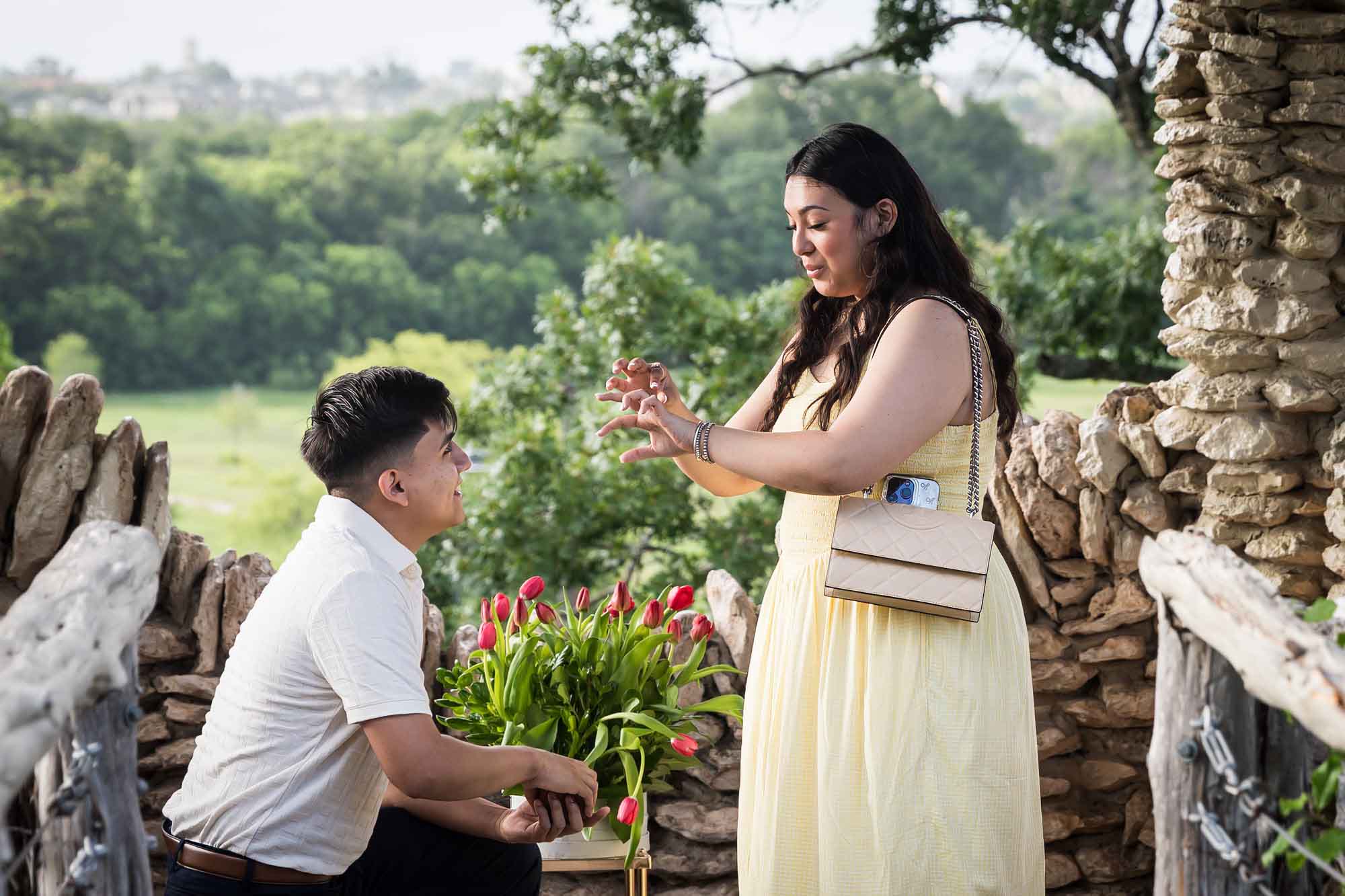Man wearing black pants bending down on one knee in front of woman wearing yellow dress in stone gazebo during proposal for an article on Japanese Tea Garden proposal tips