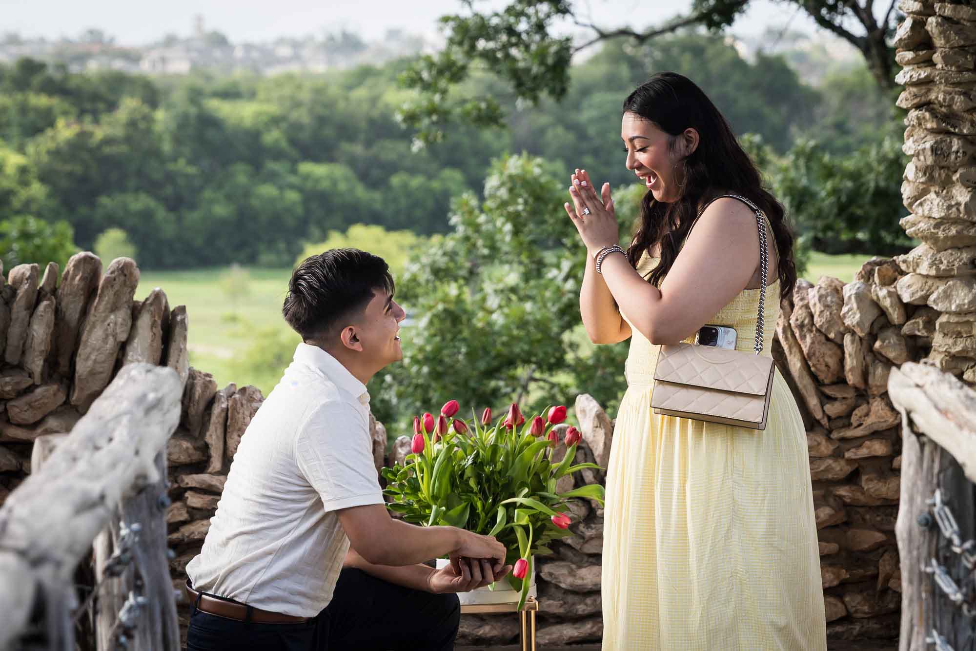 Man wearing black pants bending down on one knee in front of woman wearing yellow dress in stone gazebo during proposal for an article on Japanese Tea Garden proposal tips
