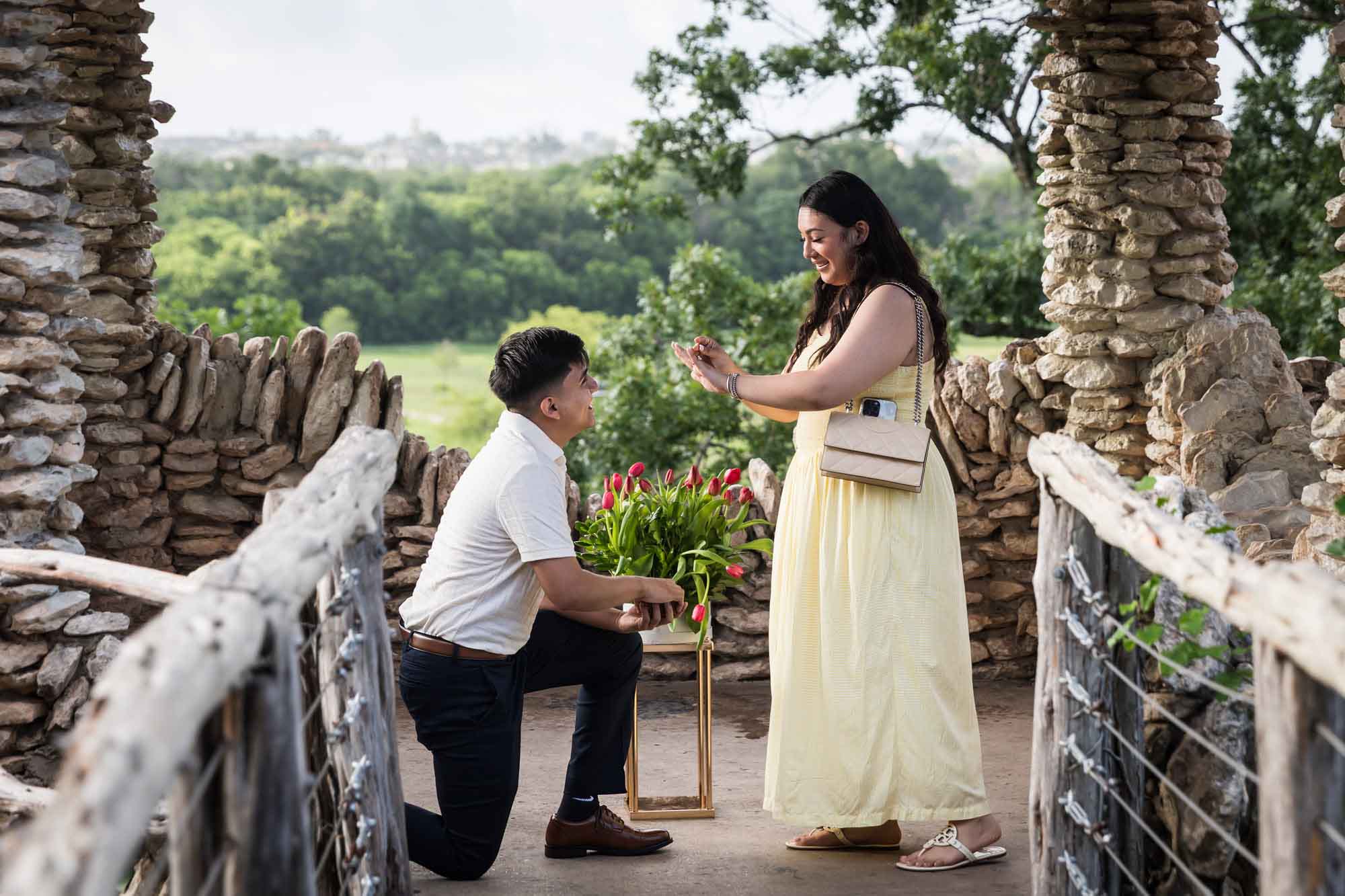 Man wearing black pants bending down on one knee in front of woman wearing yellow dress in stone gazebo during proposal for an article on Japanese Tea Garden proposal tips