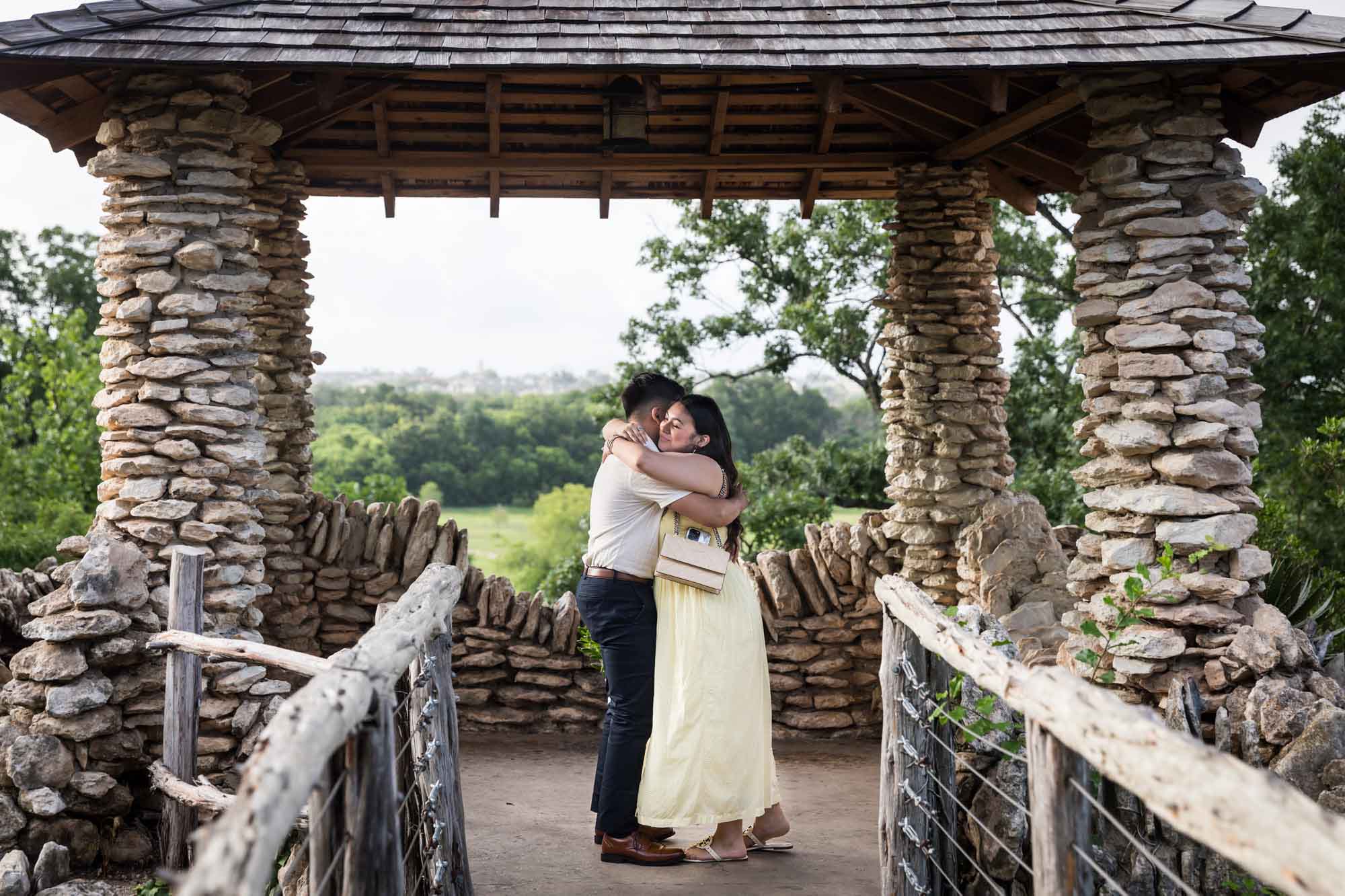 Man wearing black pants hugging woman wearing yellow dress in stone gazebo during proposal for an article on Japanese Tea Garden proposal tips