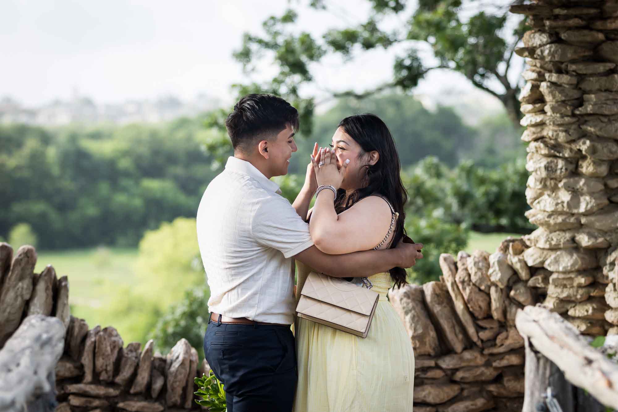 Man wearing black pants hugging woman wearing yellow dress in stone gazebo during proposal for an article on Japanese Tea Garden proposal tips