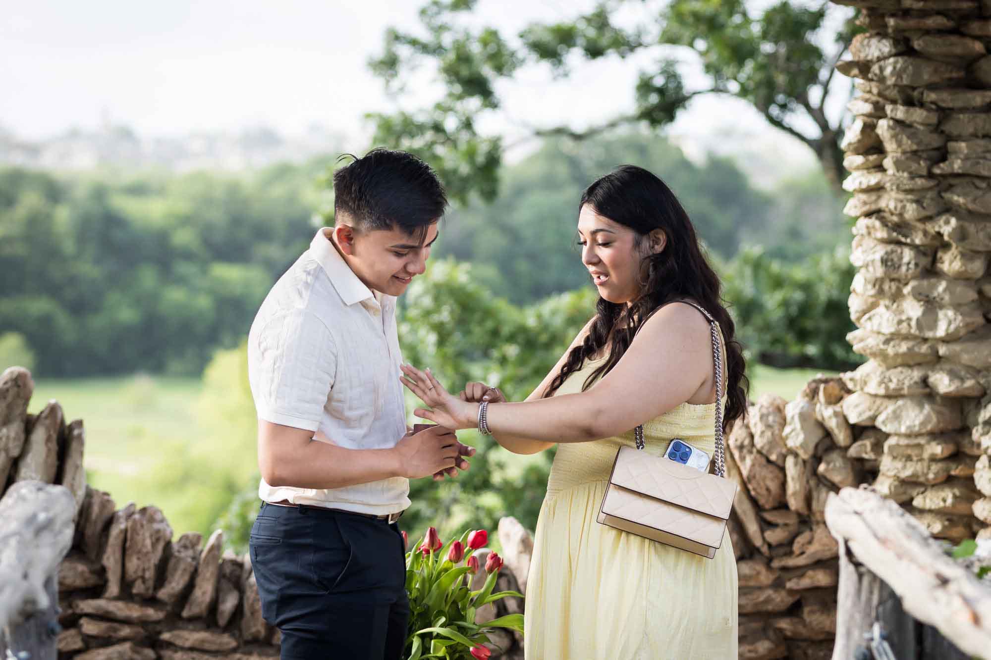 Man wearing black pants and woman wearing yellow dress looking at hand in stone gazebo during proposal for an article on Japanese Tea Garden proposal tips