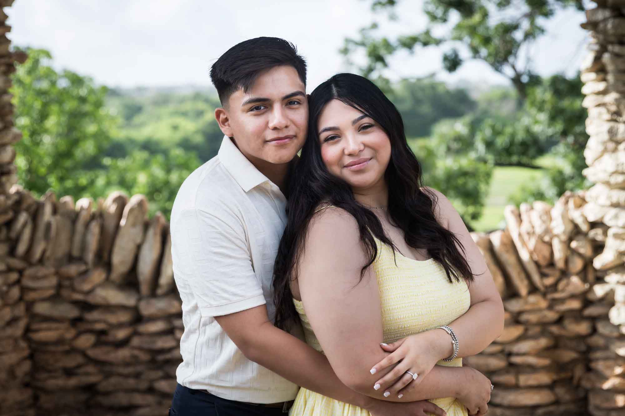 Man wearing white shirt hugging woman wearing yellow dress during a Japanese Tea Garden engagement portrait