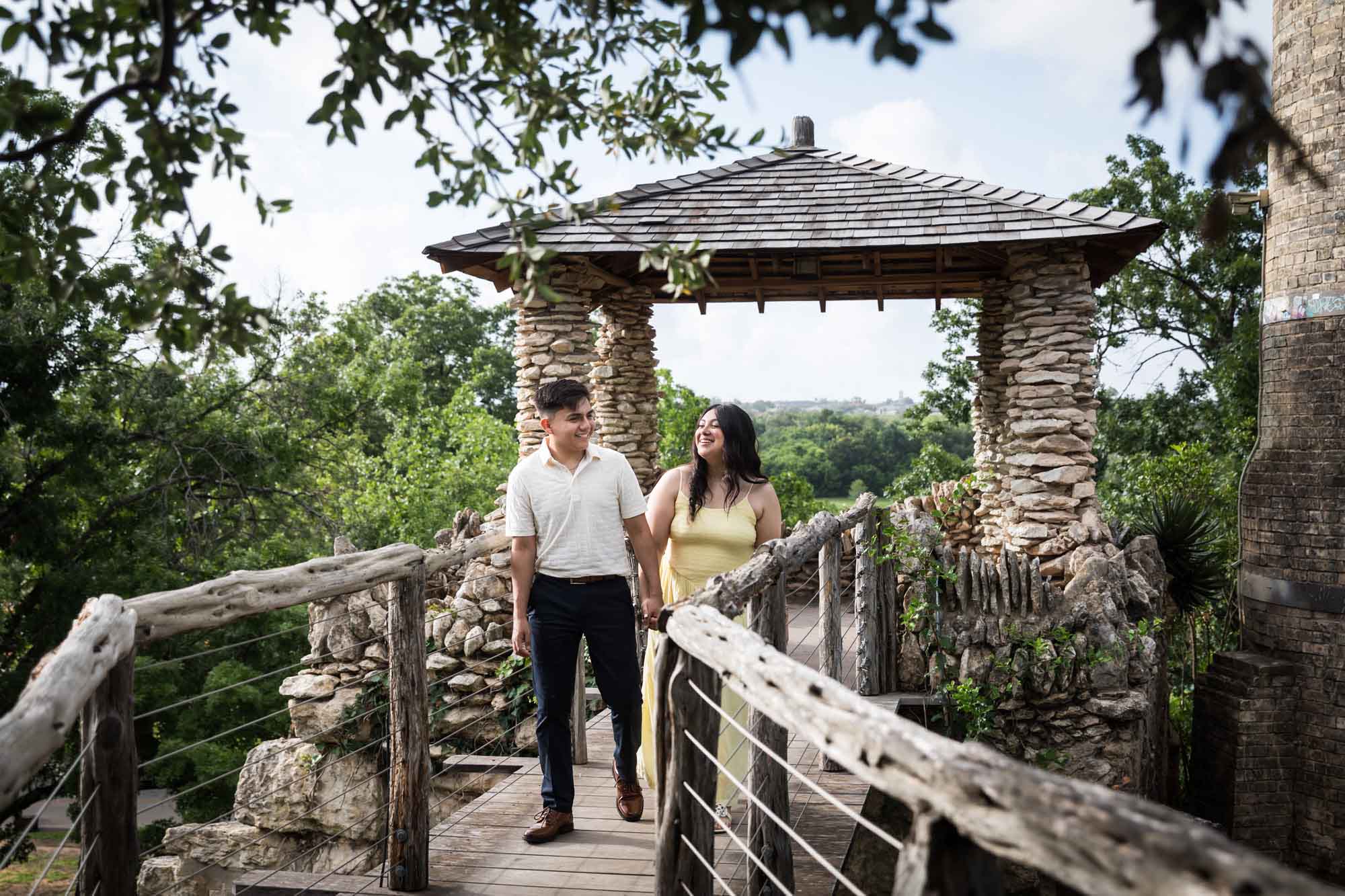 Man wearing white shirt walking down wooden pathway with woman wearing yellow dress during a Japanese Tea Garden engagement portrait
