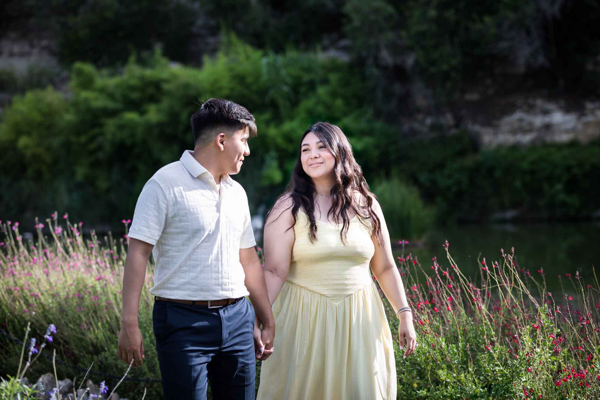 Man wearing white shirt walking down garden pathway with woman wearing yellow dress during a Japanese Tea Garden engagement portrait