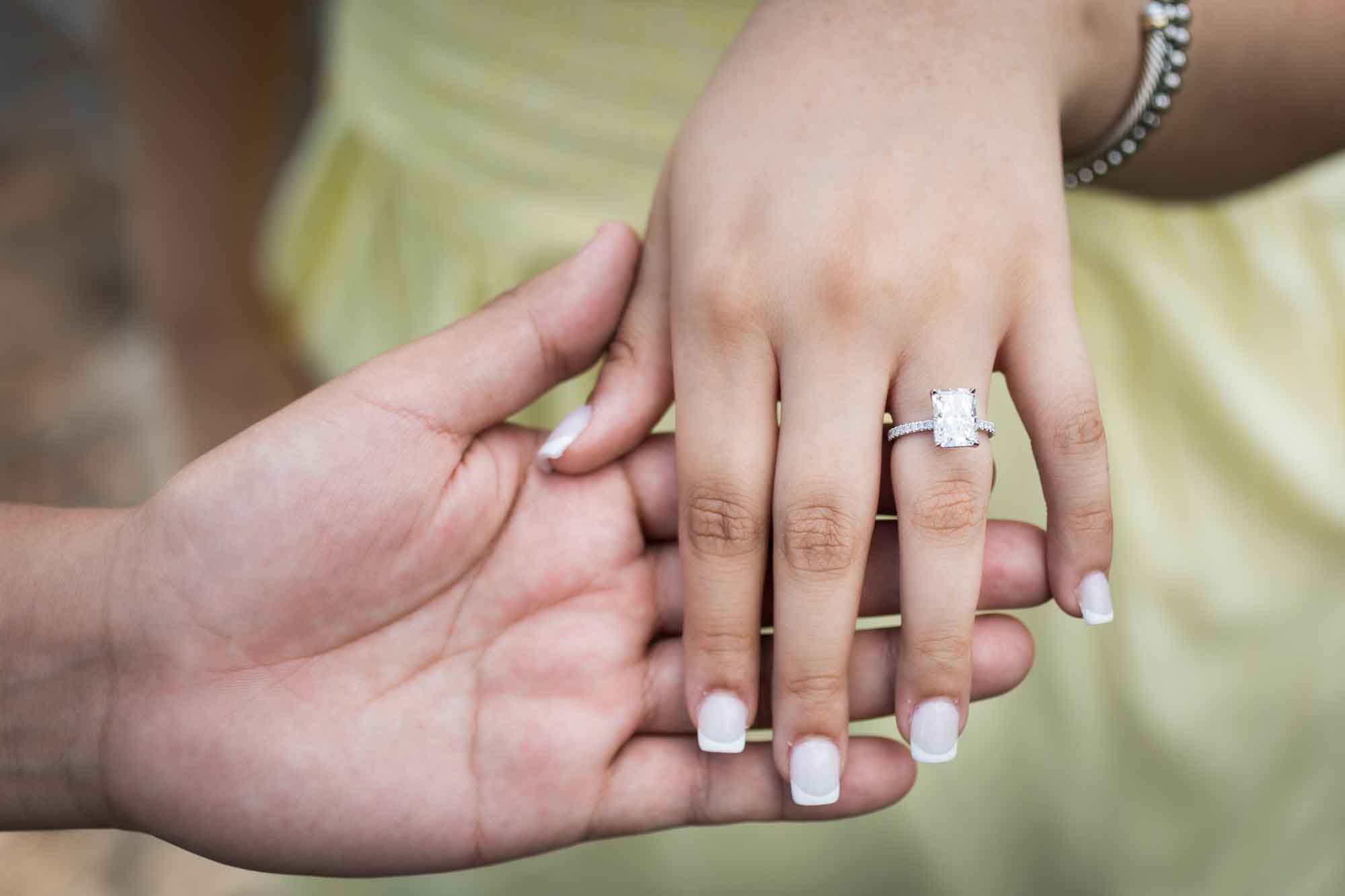 Close up of man's hand holding woman's hand showing engagement ring
