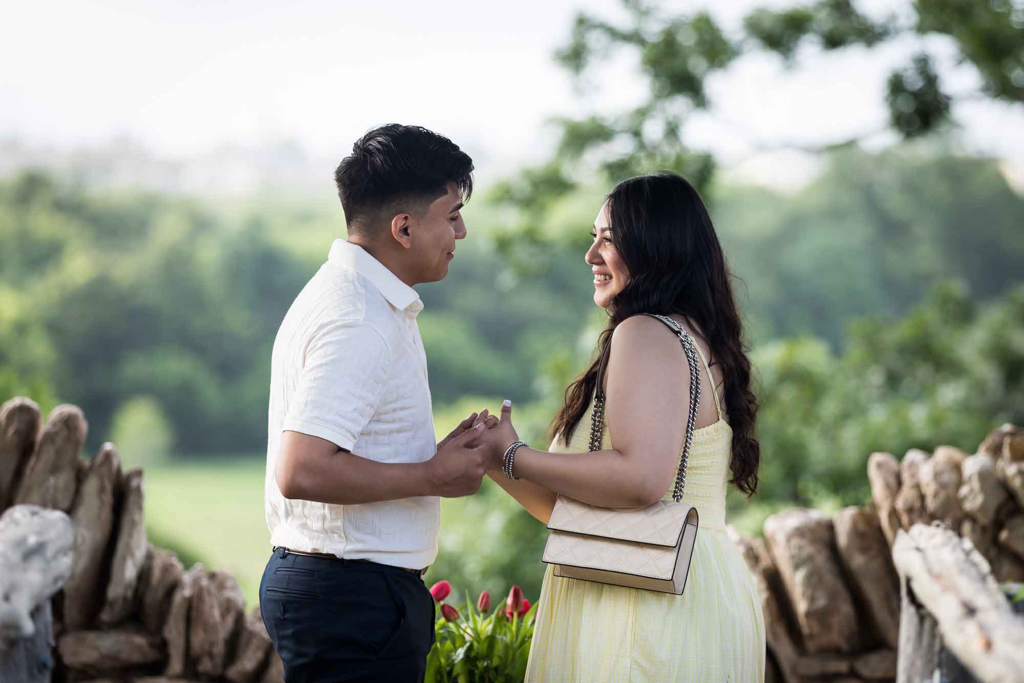 Man wearing black pants holding hands of woman wearing yellow dress in stone gazebo during proposal for an article on Japanese Tea Garden proposal tips