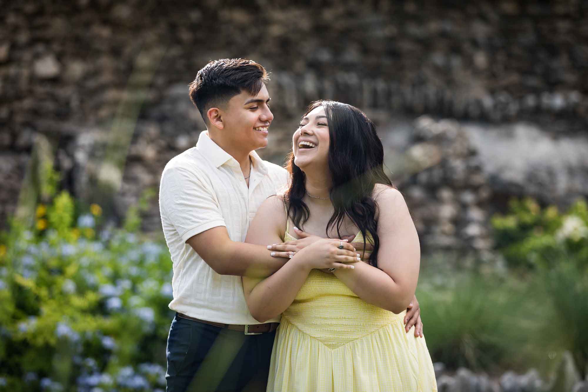 Man wearing white shirt hugging woman wearing yellow dress during a Japanese Tea Garden engagement portrait