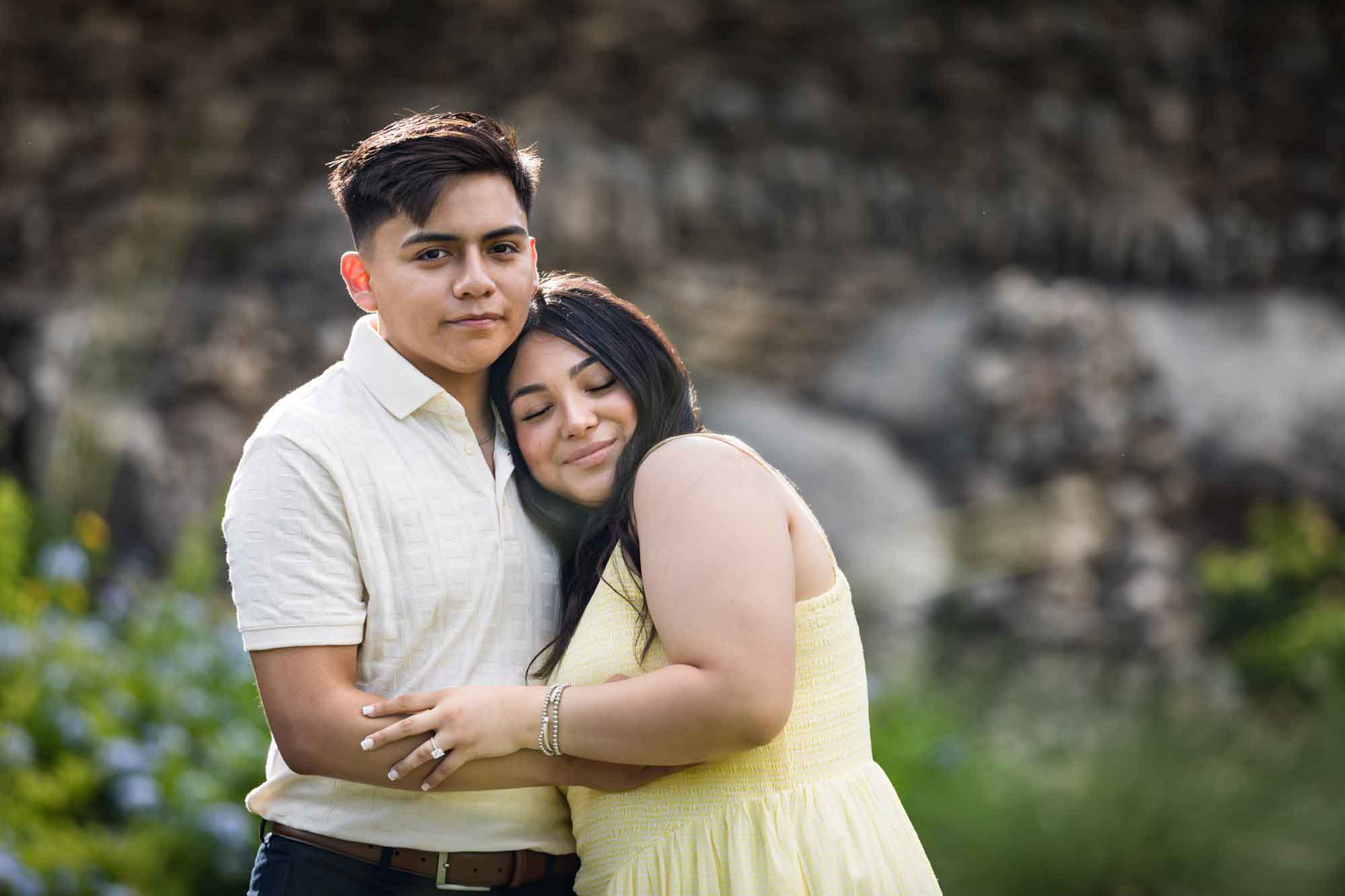 Man wearing white shirt hugging woman wearing yellow dress during a Japanese Tea Garden engagement portrait