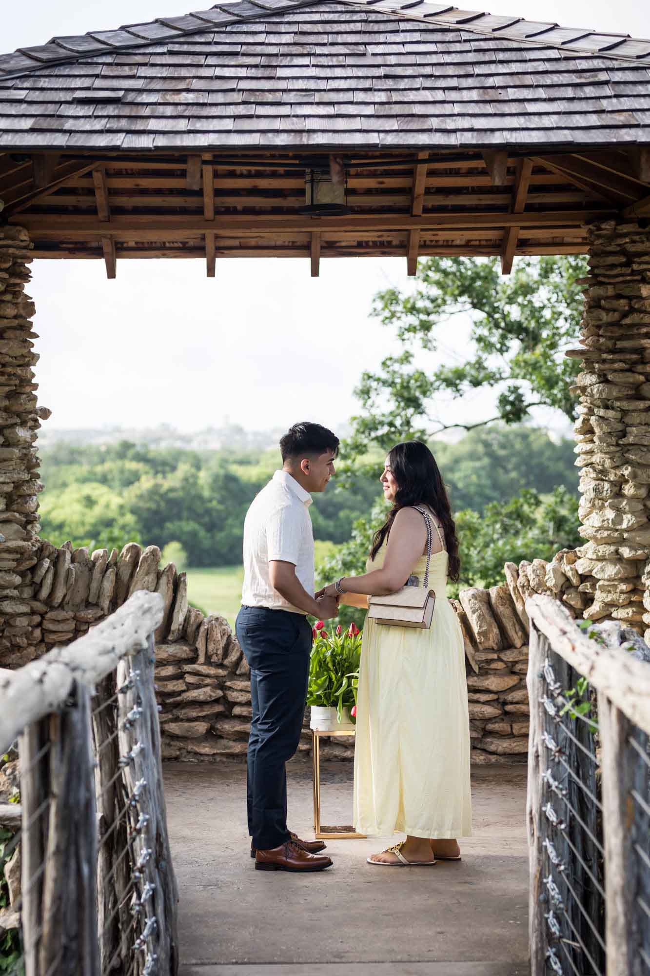 Man wearing black pants holding hands of woman wearing yellow dress in stone gazebo during proposal for an article on Japanese Tea Garden proposal tips